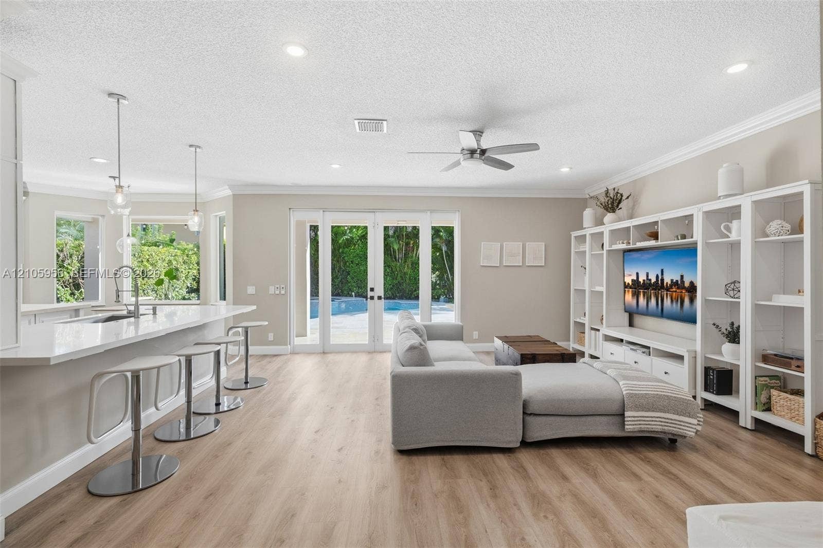 1154 Croton Court, Weston, Weston, FL 33327 Open-concept living space featuring wood-finish flooring, recessed lighting, a built-in entertainment center, a kitchen island with stone-surface countertops, and glass-paneled double doors