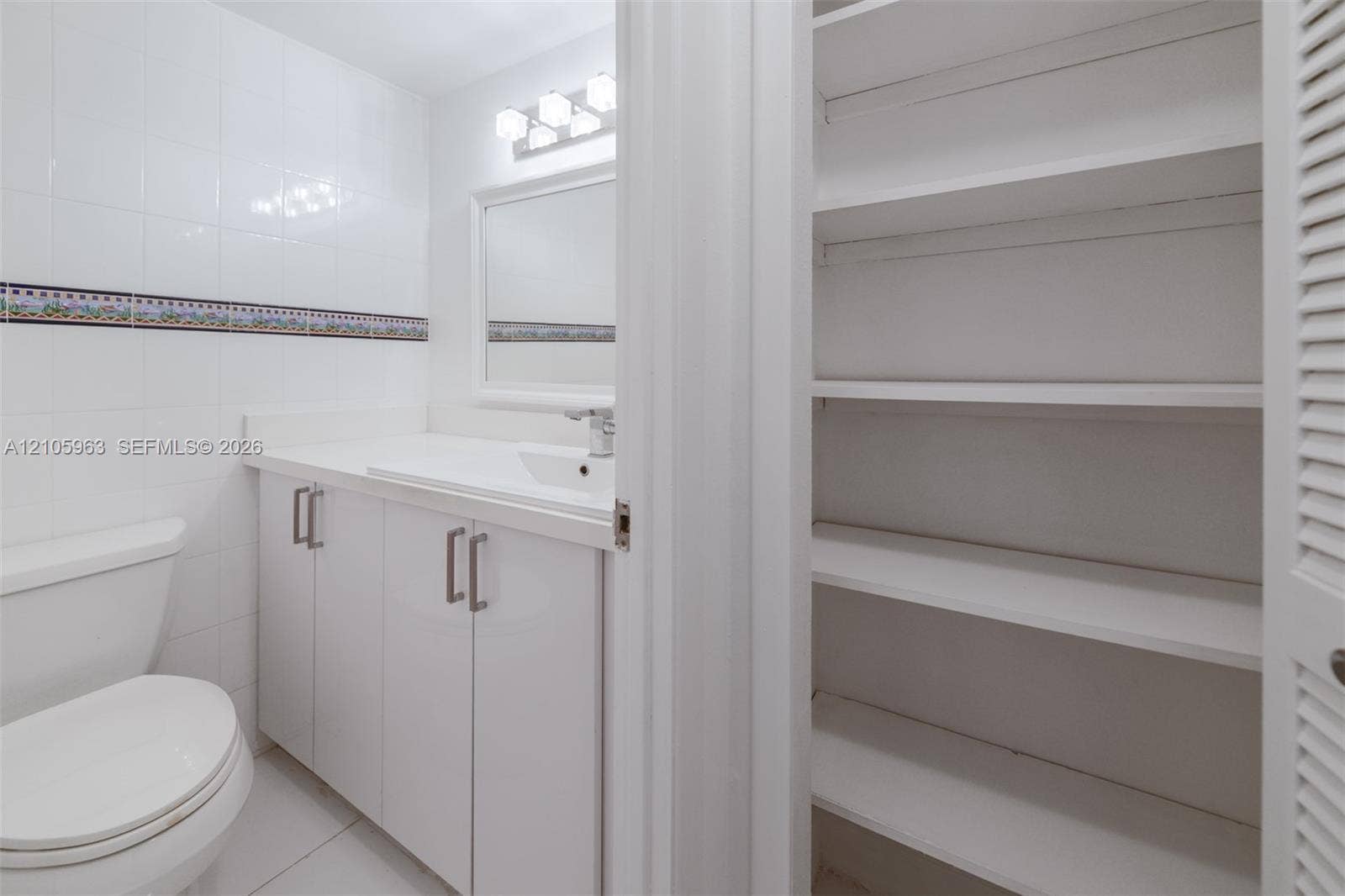 1980 S Ocean Drive, #PHA, Hallandale Beach, Hallandale Beach, FL 33009 Bathroom featuring white cabinetry, integrated sink, wall-mounted mirror, ceramic tile walls with decorative border, and built-in shelving with louvered doors
