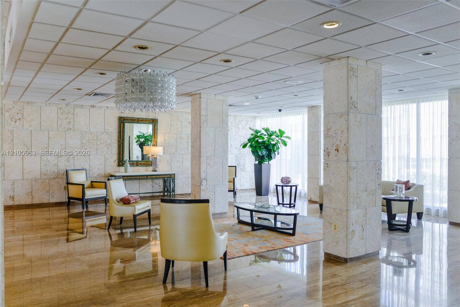 1980 S Ocean Drive, #PHA, Hallandale Beach, Hallandale Beach, FL 33009 Expansive common area featuring polished stone flooring, grid-patterned stone wall cladding, prominent structural stone pillars, recessed ceiling lighting, and a tiered crystal chandelier