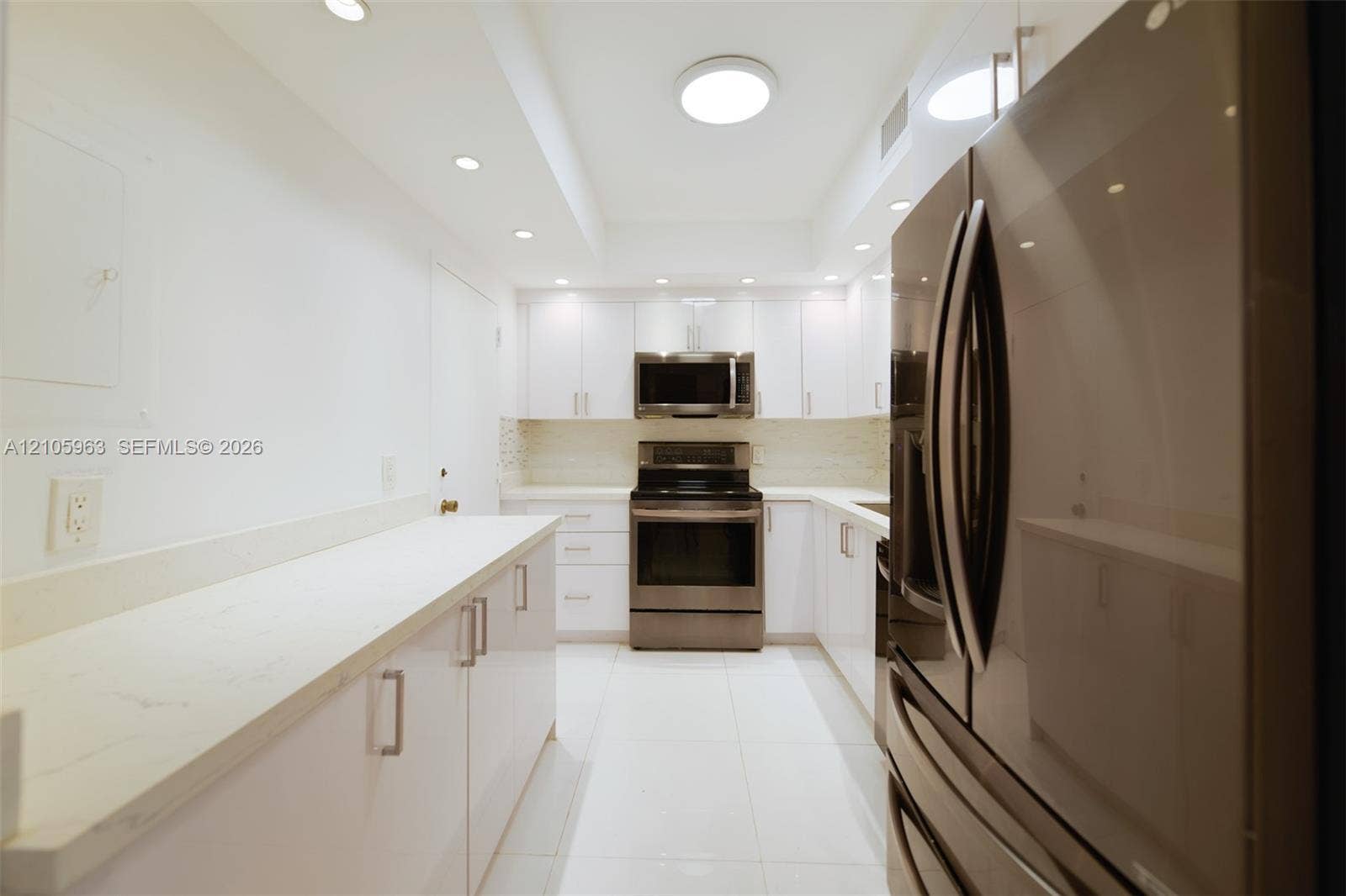 1980 S Ocean Drive, #PHA, Hallandale Beach, Hallandale Beach, FL 33009 Galley kitchen featuring white cabinetry, light-toned stone-finish countertops, stainless steel appliances, recessed ceiling lighting, and large-format tile flooring