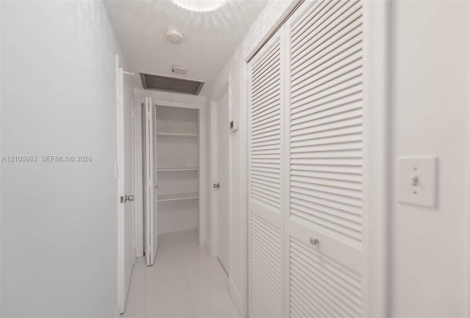 1980 S Ocean Drive, #PHA, Hallandale Beach, Hallandale Beach, FL 33009 Hallway featuring white tile flooring, ceiling-mounted light fixture, and multiple sets of white louvered doors providing built-in storage