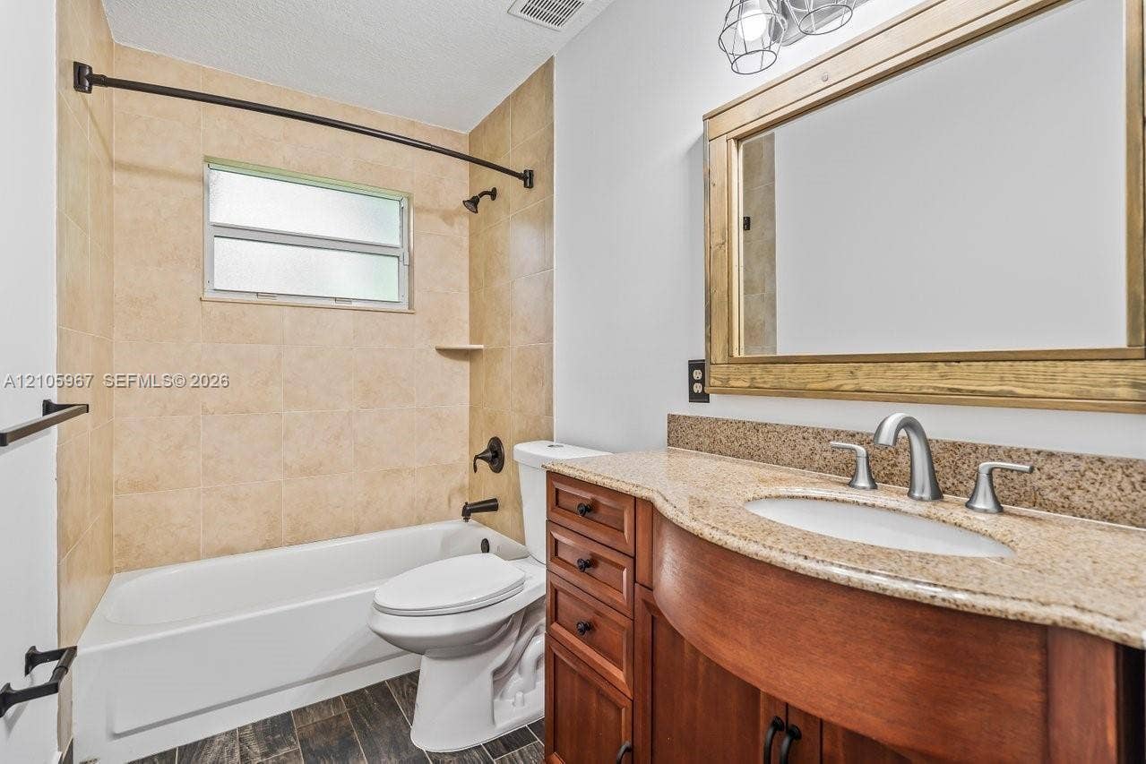 5966 NW 77th Terrace, Parkland, Parkland, FL 33067 Bathroom featuring a vanity with wood cabinetry, a stone-finish countertop, integrated basin, and brushed-finish hardware, paired with tile-surround tub-shower combination and dark wood-finish flooring