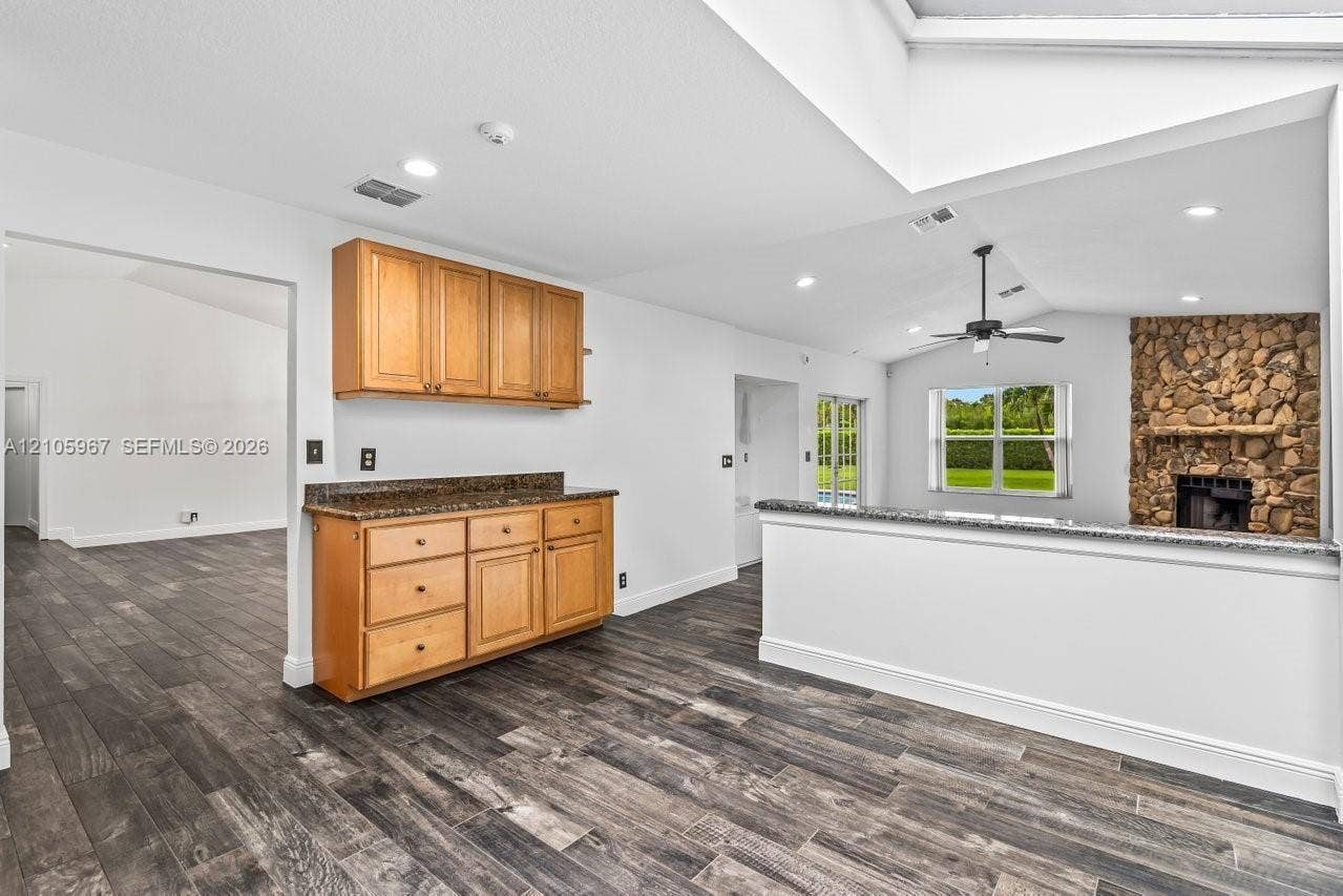 5966 NW 77th Terrace, Parkland, Parkland, FL 33067 Wood-finish flooring, stone-accented fireplace, vaulted ceiling, cabinetry with stone countertops, and recessed lighting