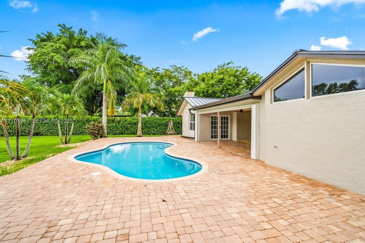 5966 NW 77th Terrace, Parkland, Parkland, FL 33067 Curved in-ground swimming pool featuring a sprawling paver patio, covered porch, and exterior accent windows