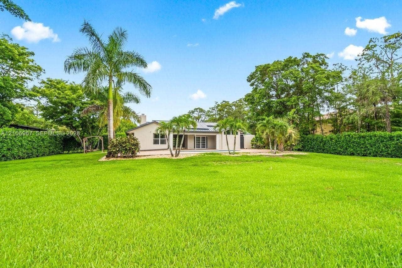 5966 NW 77th Terrace, Parkland, Parkland, FL 33067 Expansive backyard featuring a manicured lawn, perimeter hedge fencing, mature palm trees, and a light-colored exterior finish