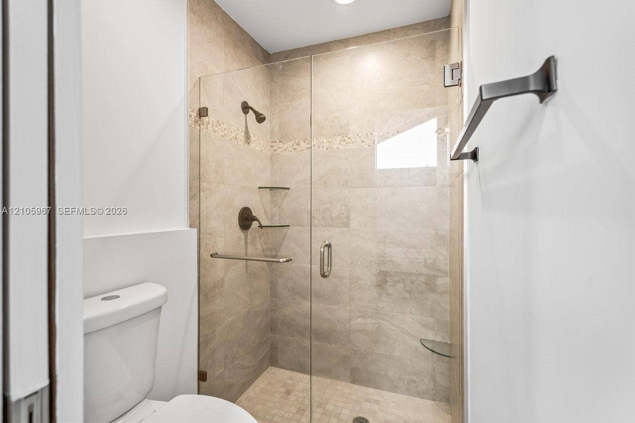 5966 NW 77th Terrace, Parkland, Parkland, FL 33067 Walk-in shower featuring glass door enclosure, neutral-toned ceramic wall tile, mosaic tile accent inlay, built-in glass shelving, and matte black hardware