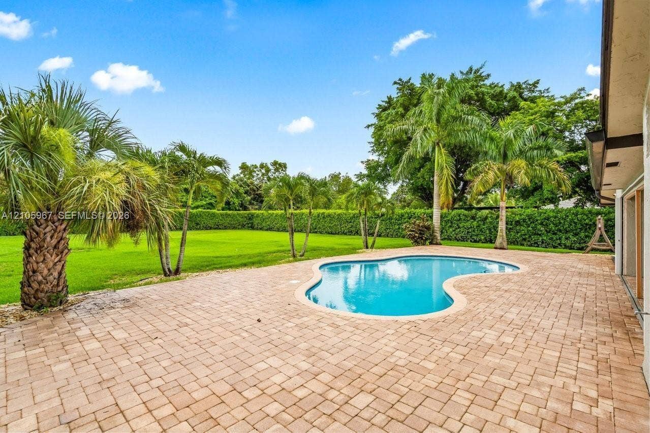 5966 NW 77th Terrace, Parkland, Parkland, FL 33067 Backyard featuring a free-form pool, expansive brick paver patio, manicured lawn, and mature perimeter landscaping