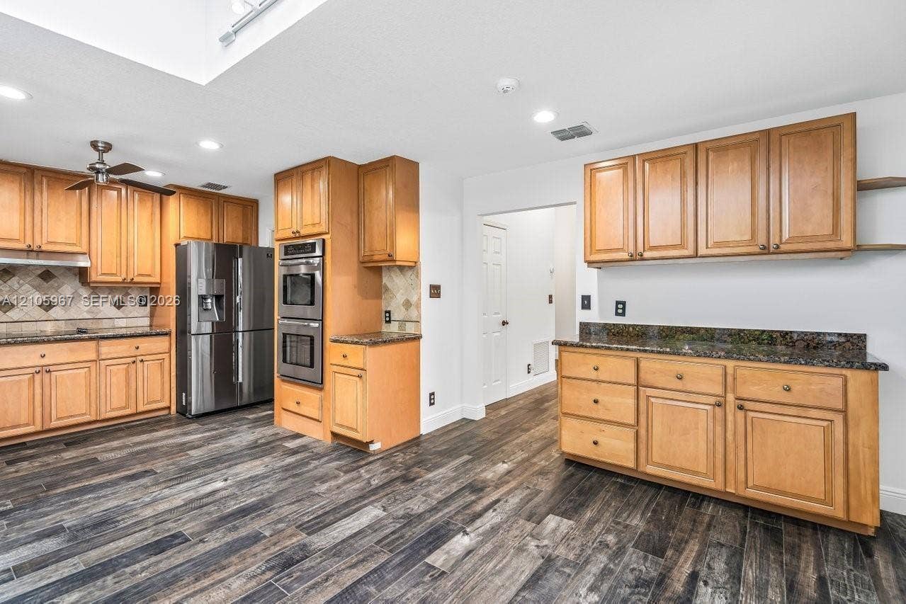5966 NW 77th Terrace, Parkland, Parkland, FL 33067 Kitchen featuring light-tone wood cabinetry, dark stone countertops, stainless steel double wall ovens, a stainless steel refrigerator, and wood-finish flooring
