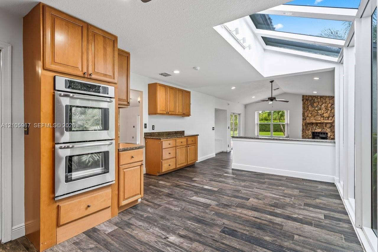 5966 NW 77th Terrace, Parkland, Parkland, FL 33067 Kitchen featuring wood-finish cabinetry, stainless steel double wall ovens, wood-finish flooring, extensive skylights, and a stone-accented fireplace