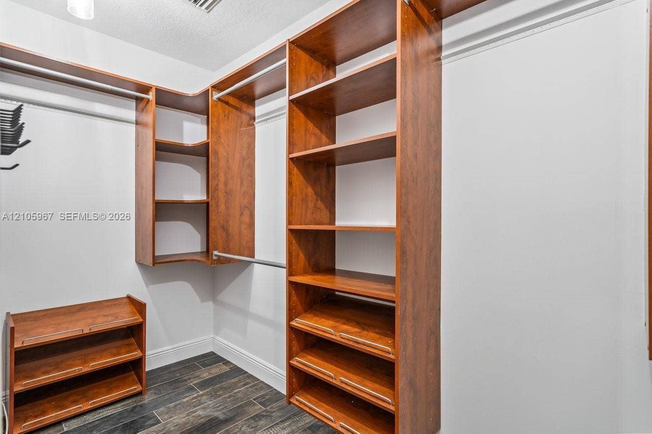 5966 NW 77th Terrace, Parkland, Parkland, FL 33067 Walk-in storage area featuring custom wood-finish shelving, integrated hanging rods, tiered shoe storage, and wood-finish flooring