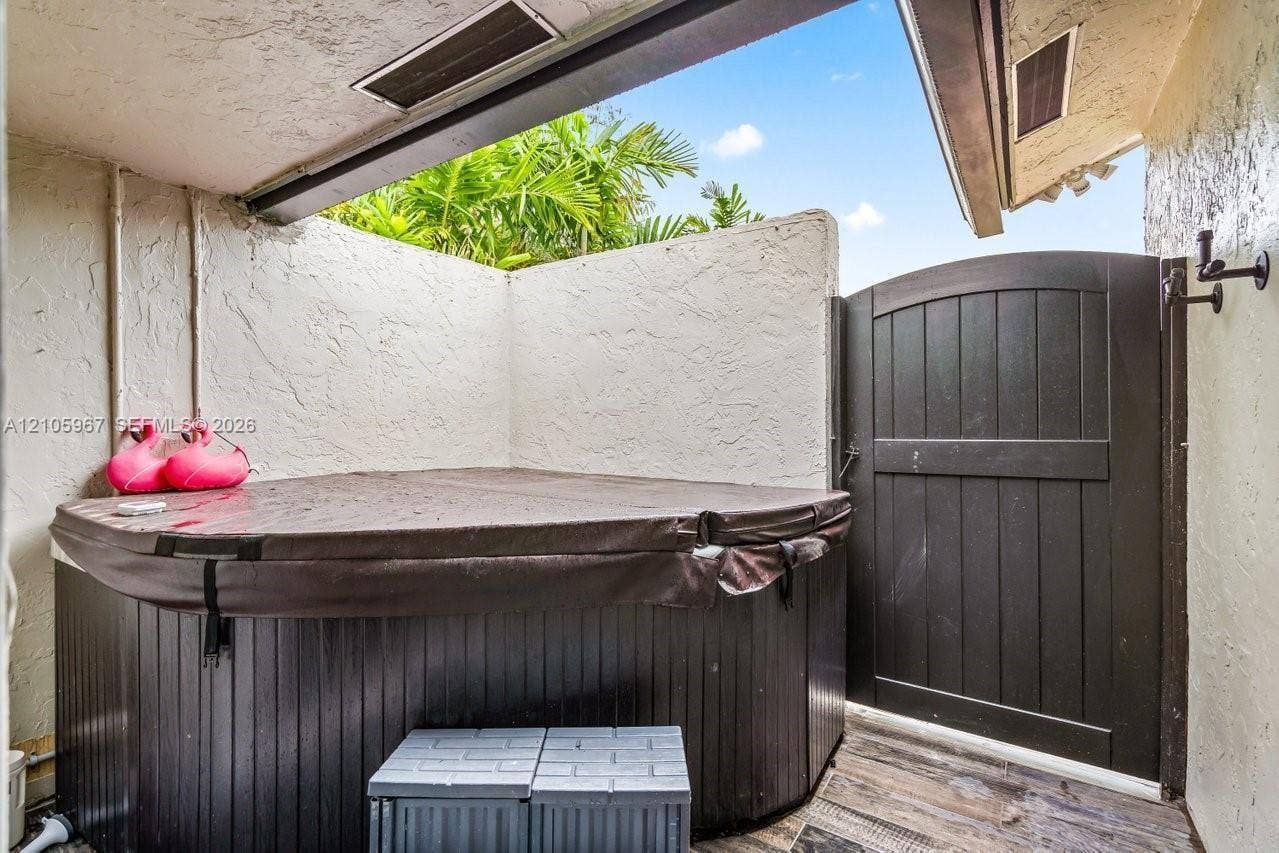 5966 NW 77th Terrace, Parkland, Parkland, FL 33067 Covered outdoor spa area featuring a wood-panel base, privacy walls with stucco finish, and an arched wooden gate
