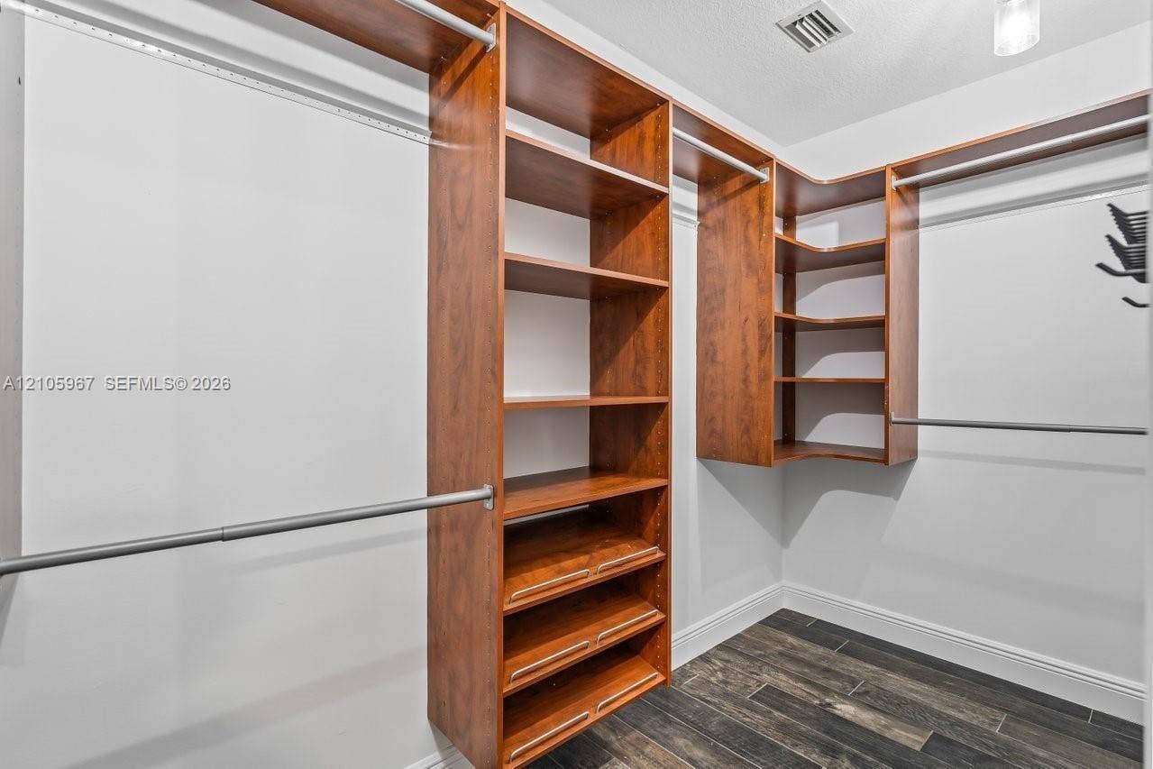 5966 NW 77th Terrace, Parkland, Parkland, FL 33067 Walk-in storage space featuring built-in wood cabinetry, adjustable shelving, integrated hanging rods, and dark wood-finish flooring