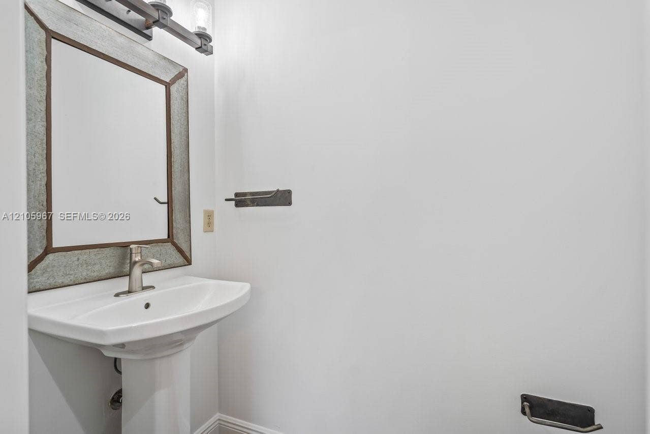 5966 NW 77th Terrace, Parkland, Parkland, FL 33067 Pedestal sink with a single-handle faucet, metal-framed wall mirror, and industrial-style wall-mounted lighting fixture