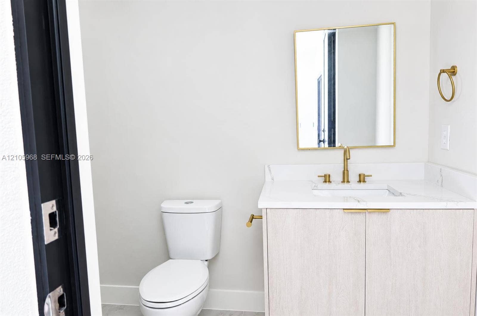 3509 63rd Street W, Lehigh Acres, FL 33971 Vanity featuring a light wood-finish cabinet, stone-surface countertop, and gold-toned hardware, accompanied by a rectangular mirror with a gold-toned frame and a gold-toned widespread faucet