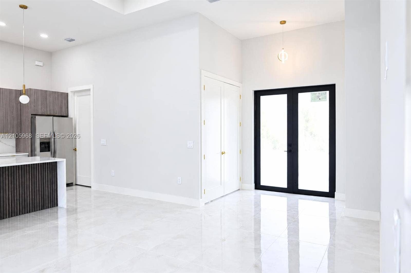 3509 63rd Street W, Lehigh Acres, FL 33971 Open-concept interior featuring large-format polished tile flooring, high ceilings, a kitchen island with vertical wood-finish paneling, custom cabinetry, and black-framed glass-paneled double doors