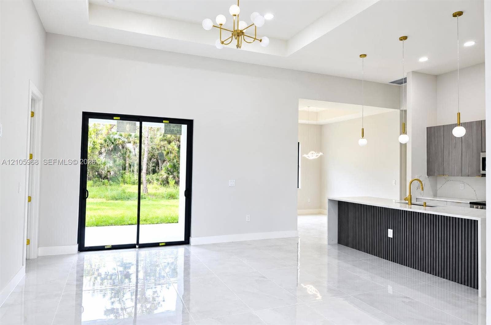 3509 63rd Street W, Lehigh Acres, FL 33971 Open floor plan featuring a coffered ceiling, large-format tile flooring, a kitchen island with a slatted base, and black-frame sliding glass doors