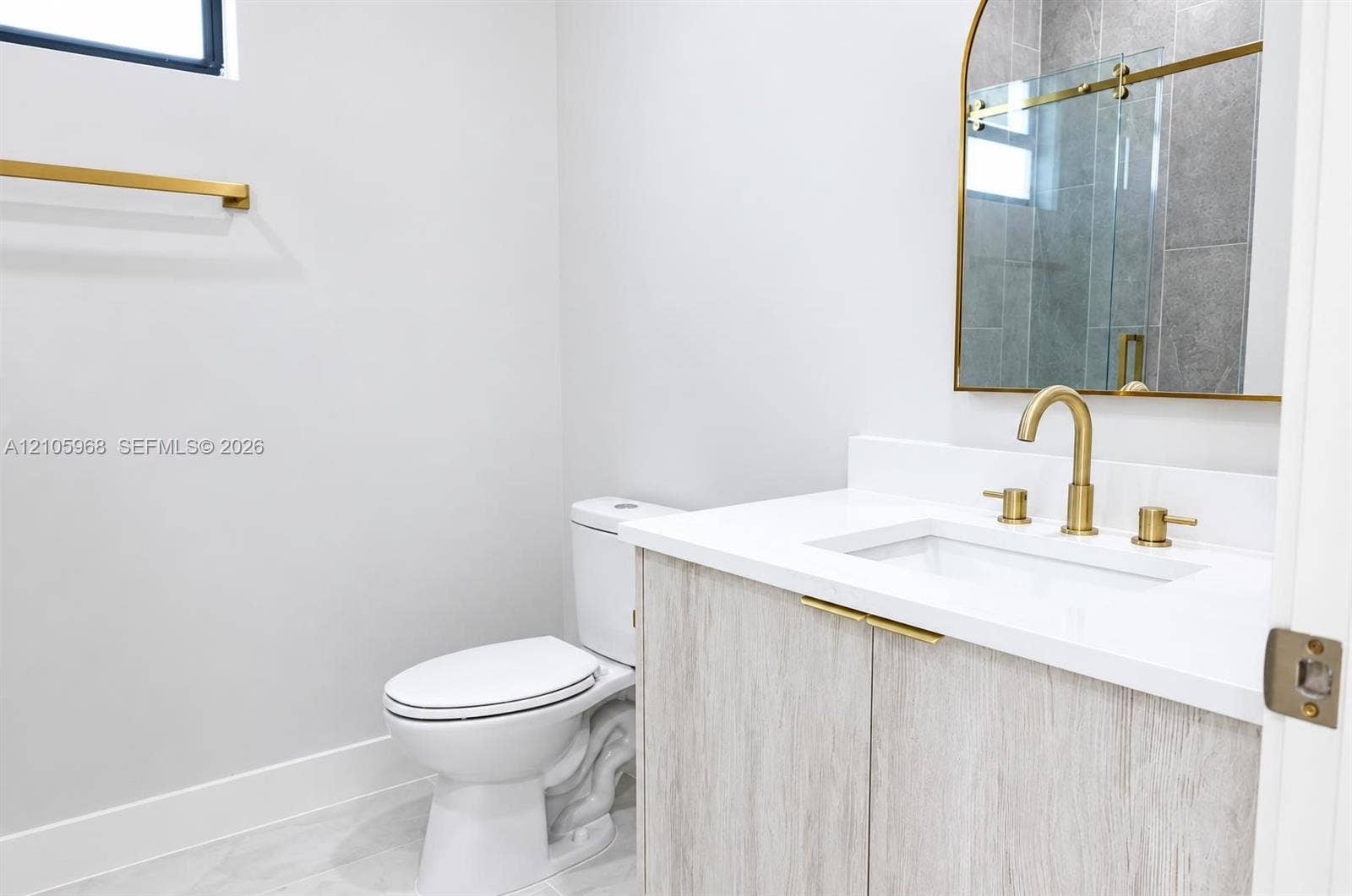 3509 63rd Street W, Lehigh Acres, FL 33971 Vanity featuring light wood-finish cabinetry, a white countertop with an integrated rectangular sink, brass hardware, an arched mirror, and a wall-mounted faucet