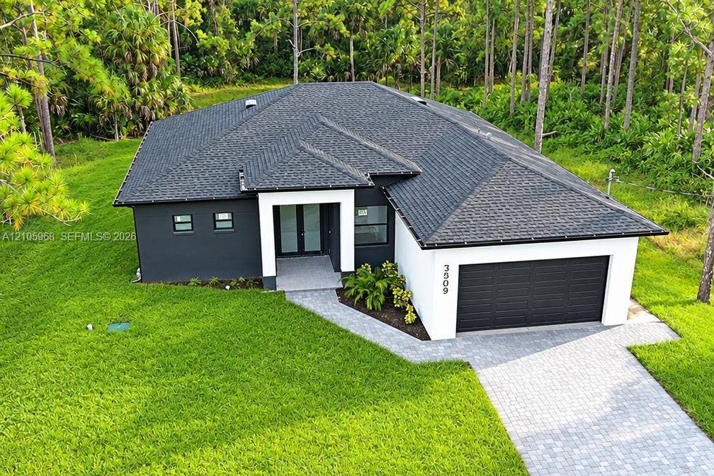 3509 63rd Street W, Lehigh Acres, FL 33971 Contemporary exterior featuring high-contrast stucco finish, shingle roofing, integrated two-car garage, and paver driveway
