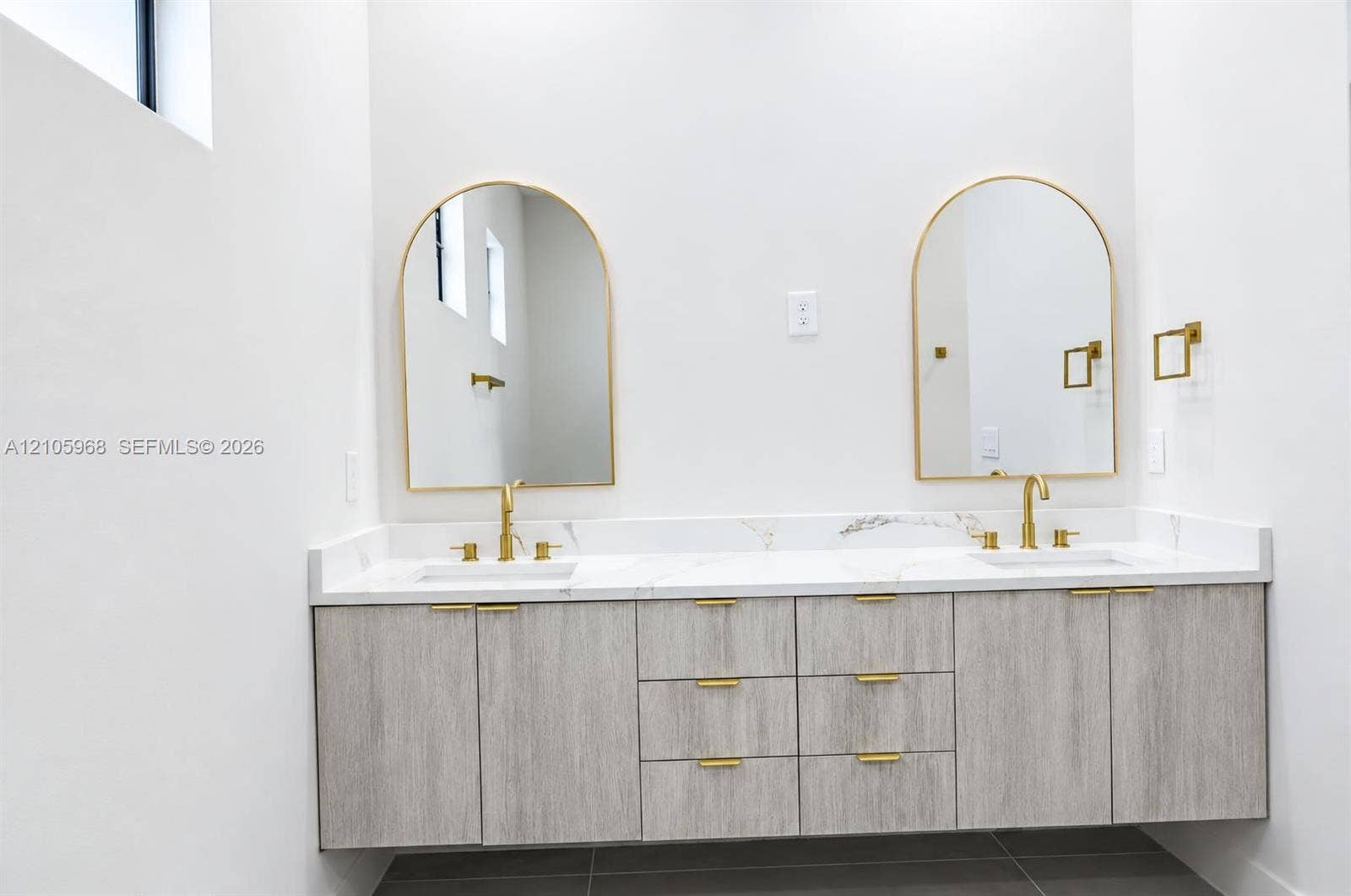 3509 63rd Street W, Lehigh Acres, FL 33971 Floating vanity with wood-finish cabinetry, dual undermount sinks, stone-surface countertop, arched mirrors, and brass-tone fixtures