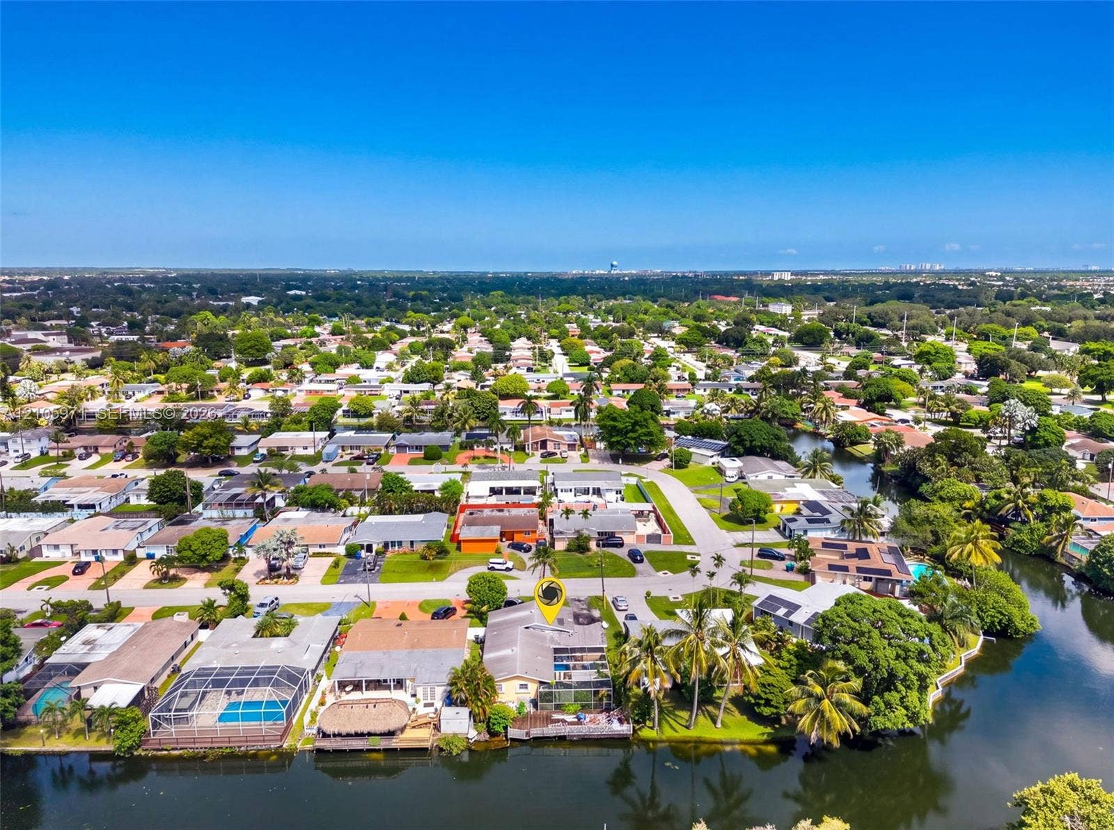 6604 Coconut Drive, Miramar, FL 33023 Aerial perspective of a waterfront property featuring a screened-in lanai, concrete seawall, mature palm trees, and direct canal access