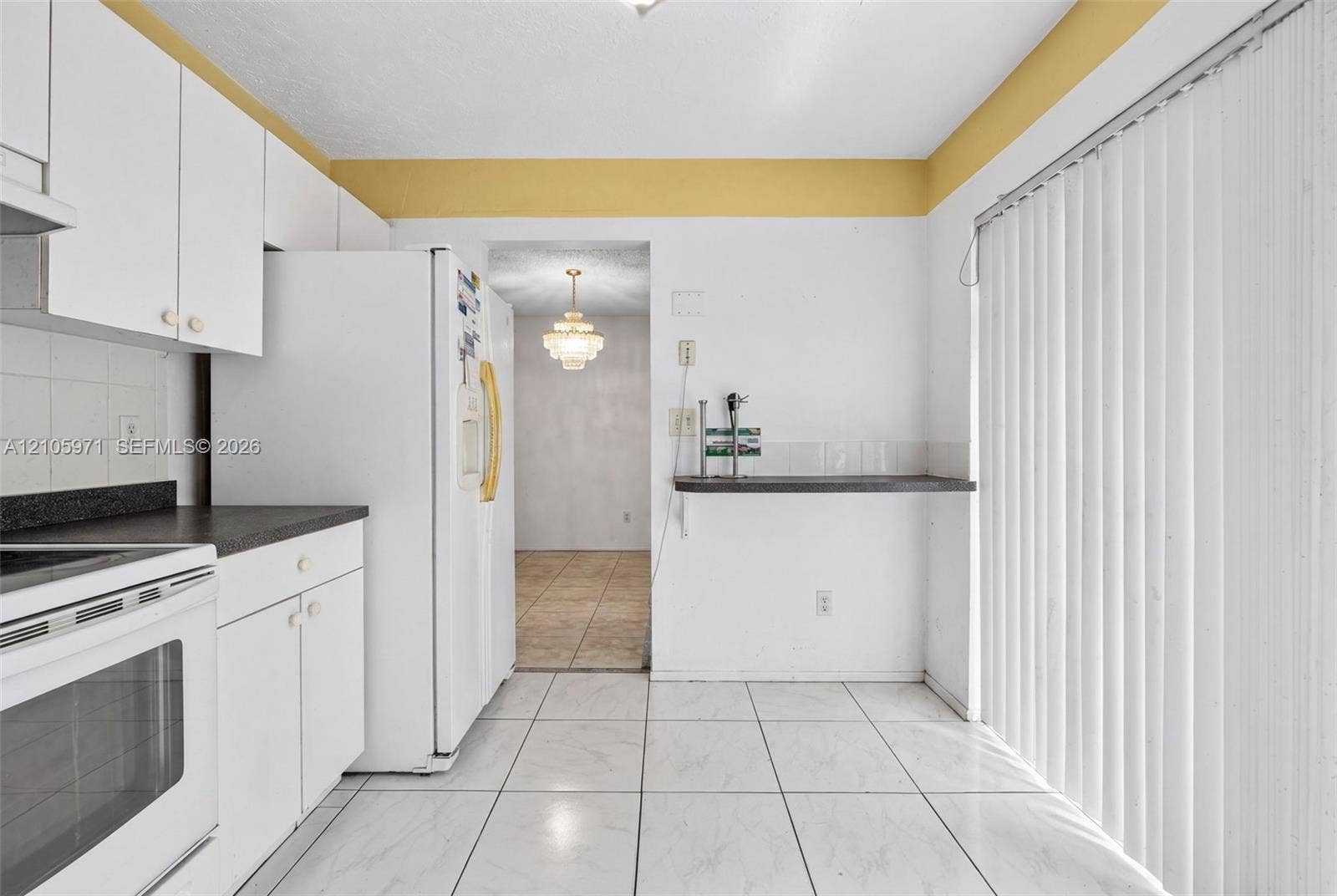 6604 Coconut Drive, Miramar, FL 33023 Kitchen featuring white cabinetry, dark countertops, tile flooring, and vertical blinds covering the sliding glass door