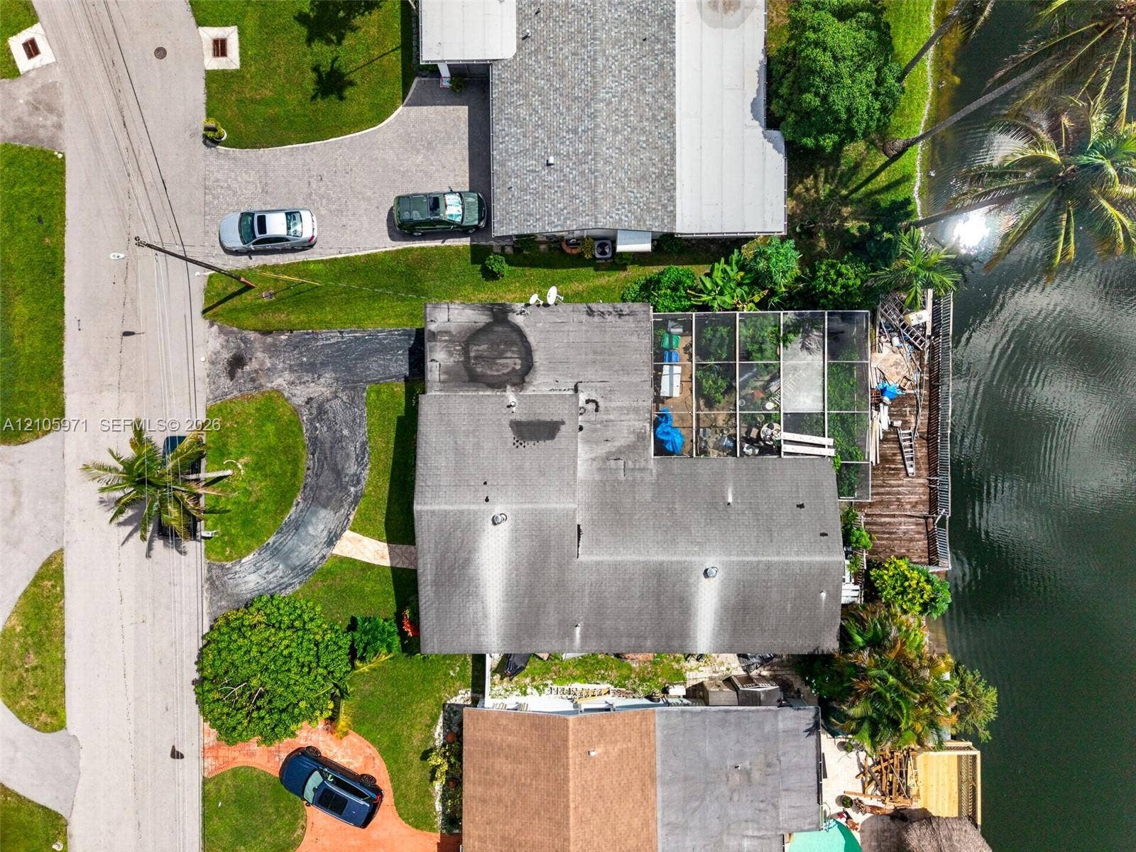 6604 Coconut Drive, Miramar, FL 33023 Aerial perspective featuring waterfront property with a screened-in lanai, asphalt driveway, and mature landscaping