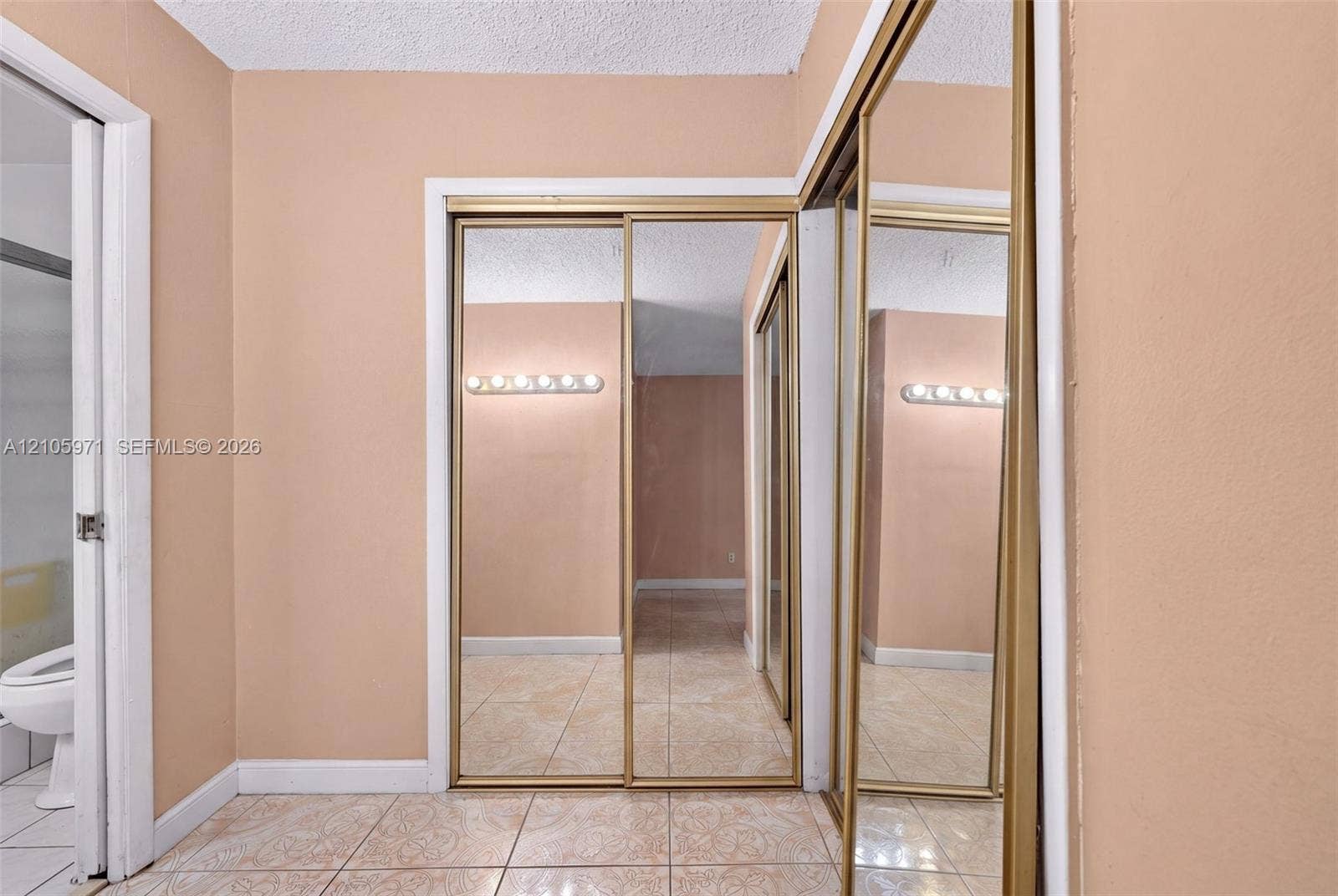 6604 Coconut Drive, Miramar, FL 33023 Floor-to-ceiling mirror-paneled sliding closet doors with gold-tone metal framing, ceramic tile flooring, and wall-mounted vanity lighting