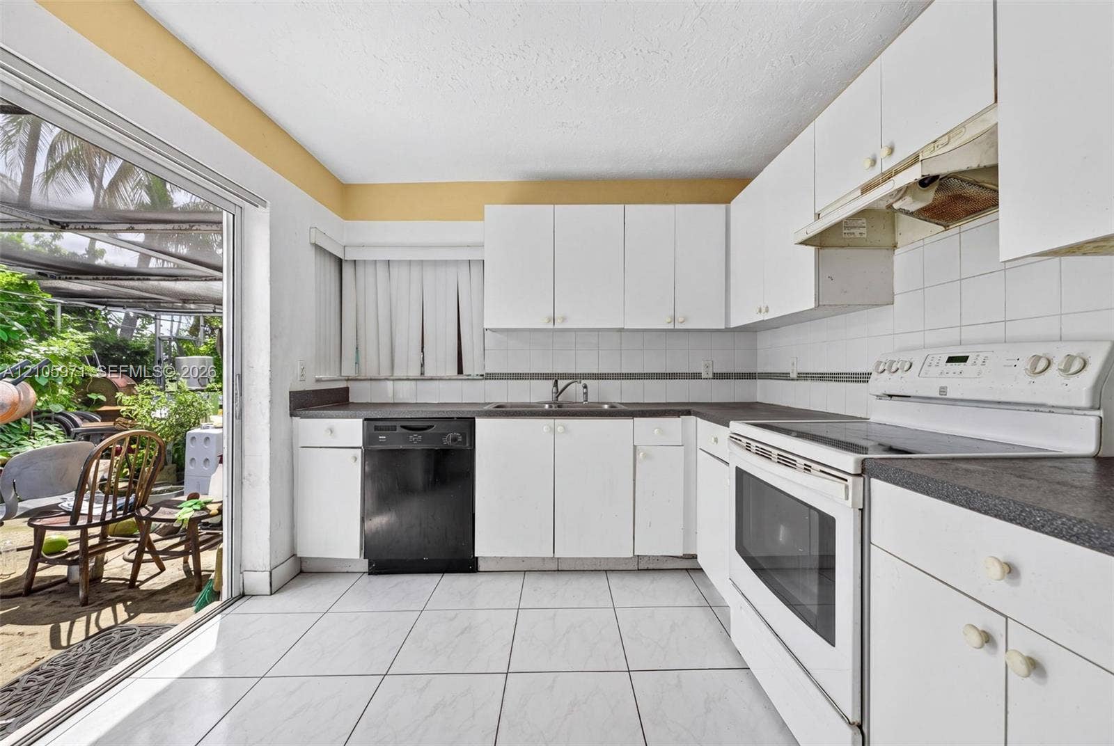 6604 Coconut Drive, Miramar, FL 33023 Kitchen featuring white cabinetry, dark countertops, a double-basin stainless steel sink, ceramic tile flooring, and a sliding glass door