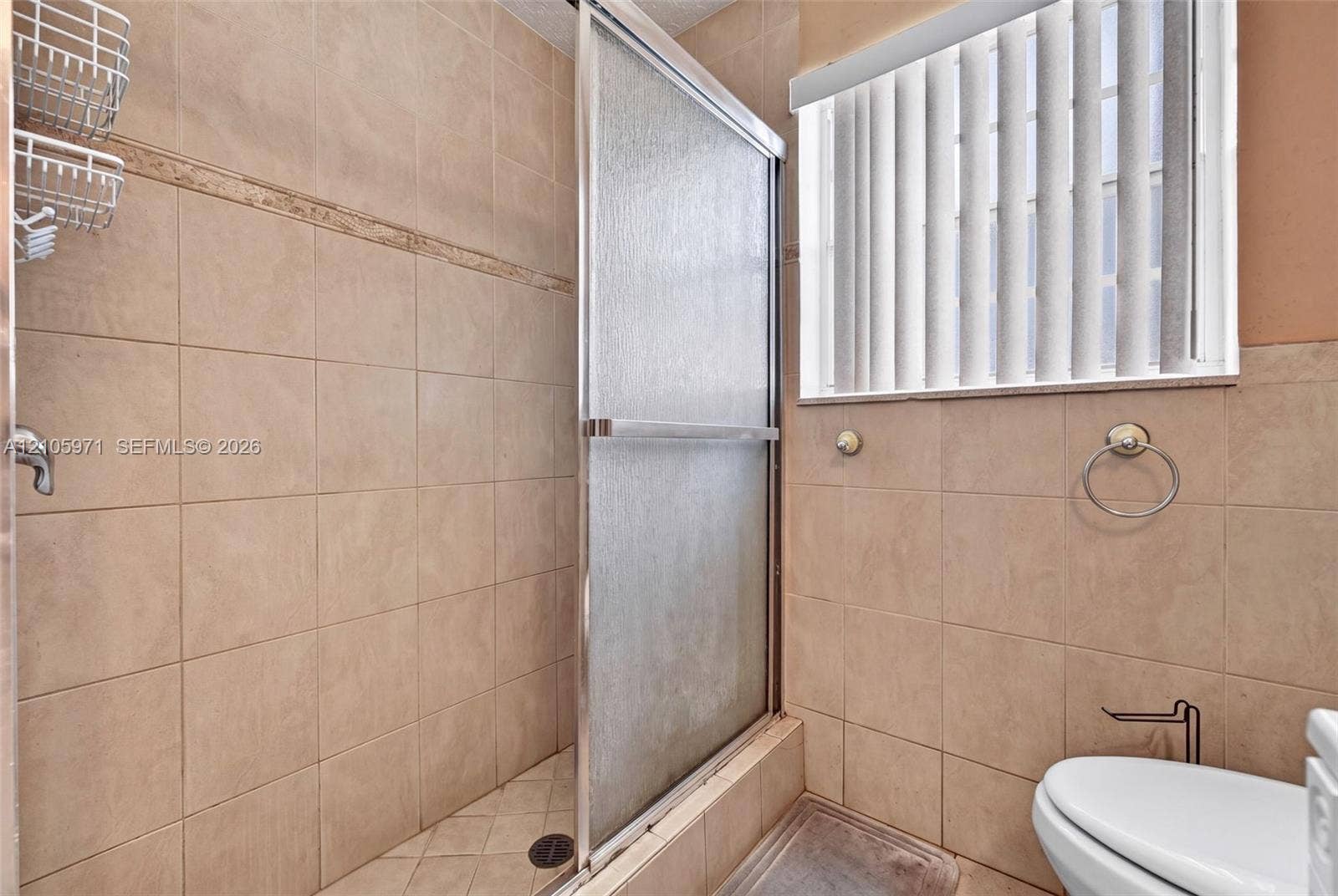 6604 Coconut Drive, Miramar, FL 33023 Tiled shower enclosure with a glass sliding door, neutral wall tile, and vertical window blinds