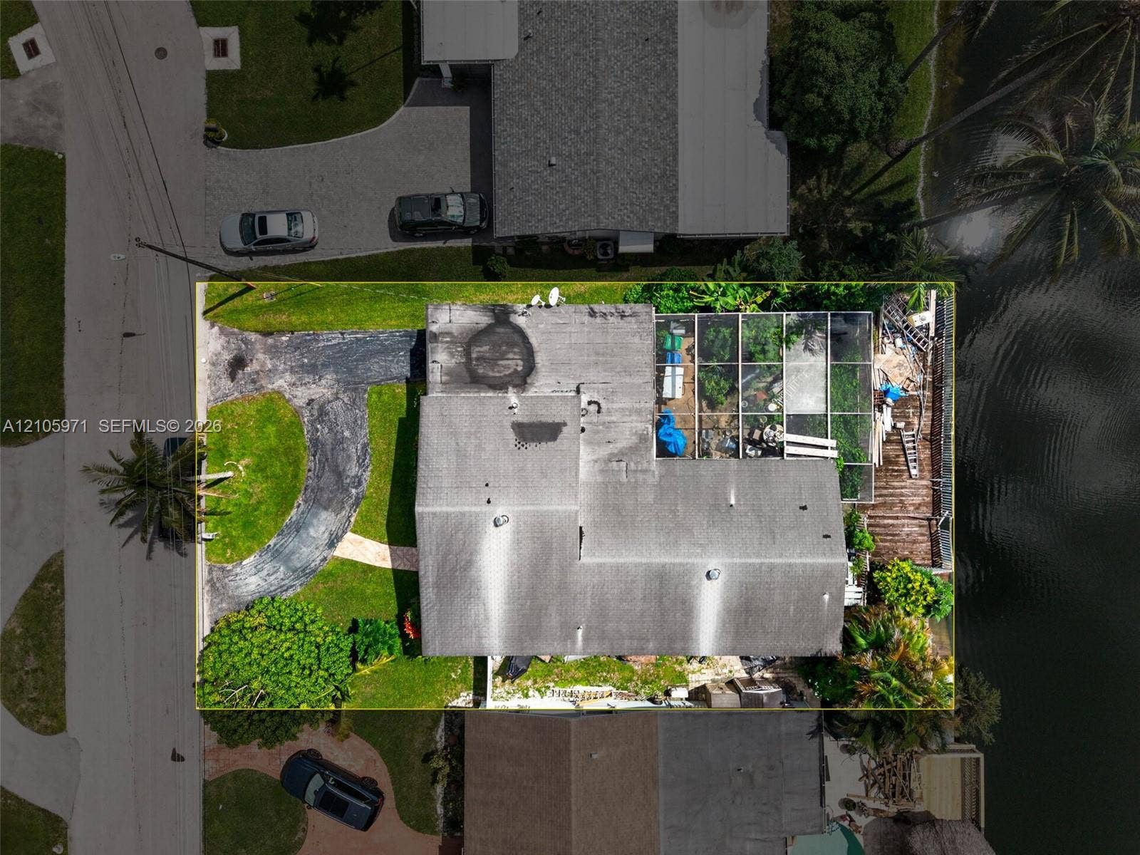 6604 Coconut Drive, Miramar, FL 33023 Aerial view of the property featuring a waterfront location, a screened lanai, a paved driveway, and mature landscaping