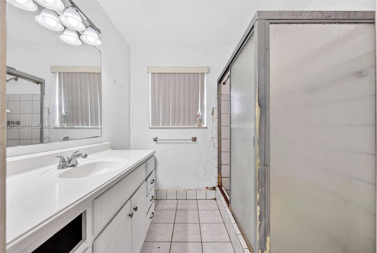 6604 Coconut Drive, Miramar, FL 33023 Bathroom featuring a white vanity with an integrated sink, polished chrome faucet, multi-bulb light fixture, tile flooring, and a glass-enclosed shower