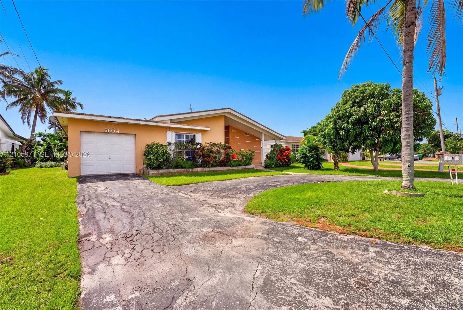 6604 Coconut Drive, Miramar, FL 33023 Single-story residence featuring a stucco exterior, attached one-car garage, and landscaped front yard with mature palms