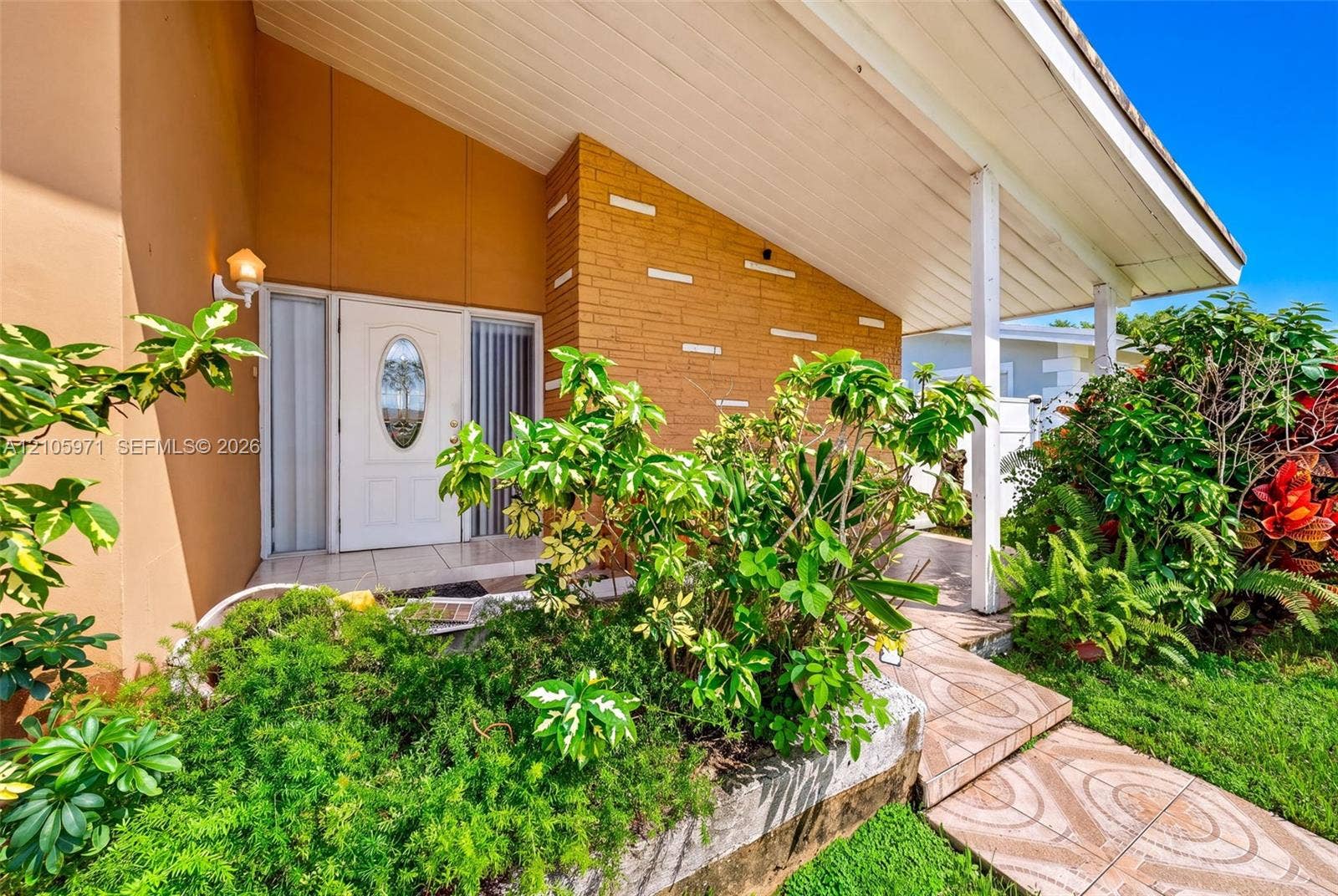 6604 Coconut Drive, Miramar, FL 33023 Mid-century modern facade featuring an exposed brick exterior wall, a covered entryway, a glass-panel front door with an oval window, and decorative horizontal masonry detailing