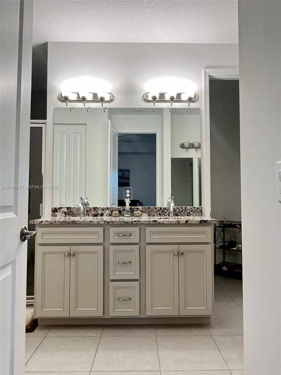 6220 Oceanaire Way, Lake Worth, FL 33467 Double-sink vanity featuring neutral-toned cabinetry, a stone-patterned countertop, a large wall-mounted mirror, and dual light fixtures