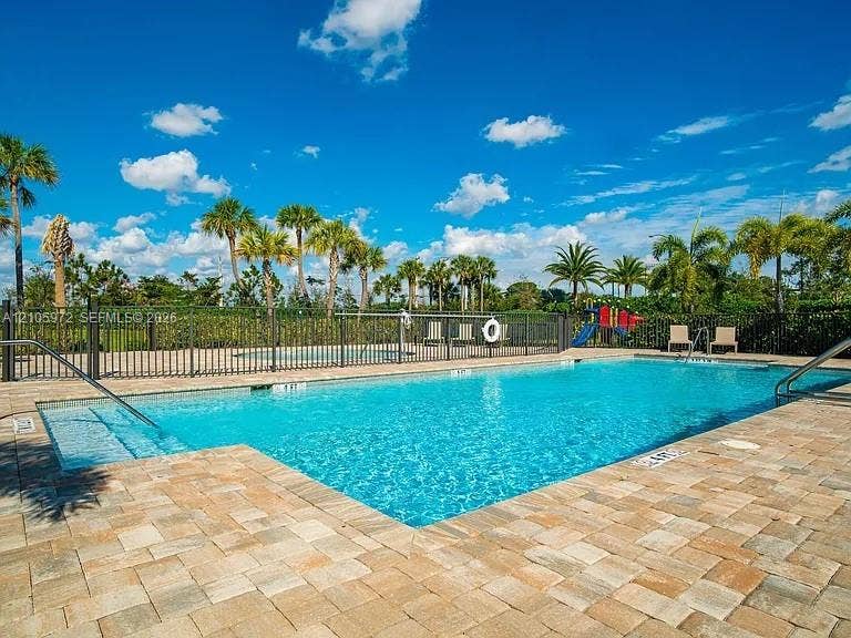 6220 Oceanaire Way, Lake Worth, FL 33467 In-ground swimming pool featuring a brick paver deck, built-in entry steps, metal perimeter fencing, and mature palm trees