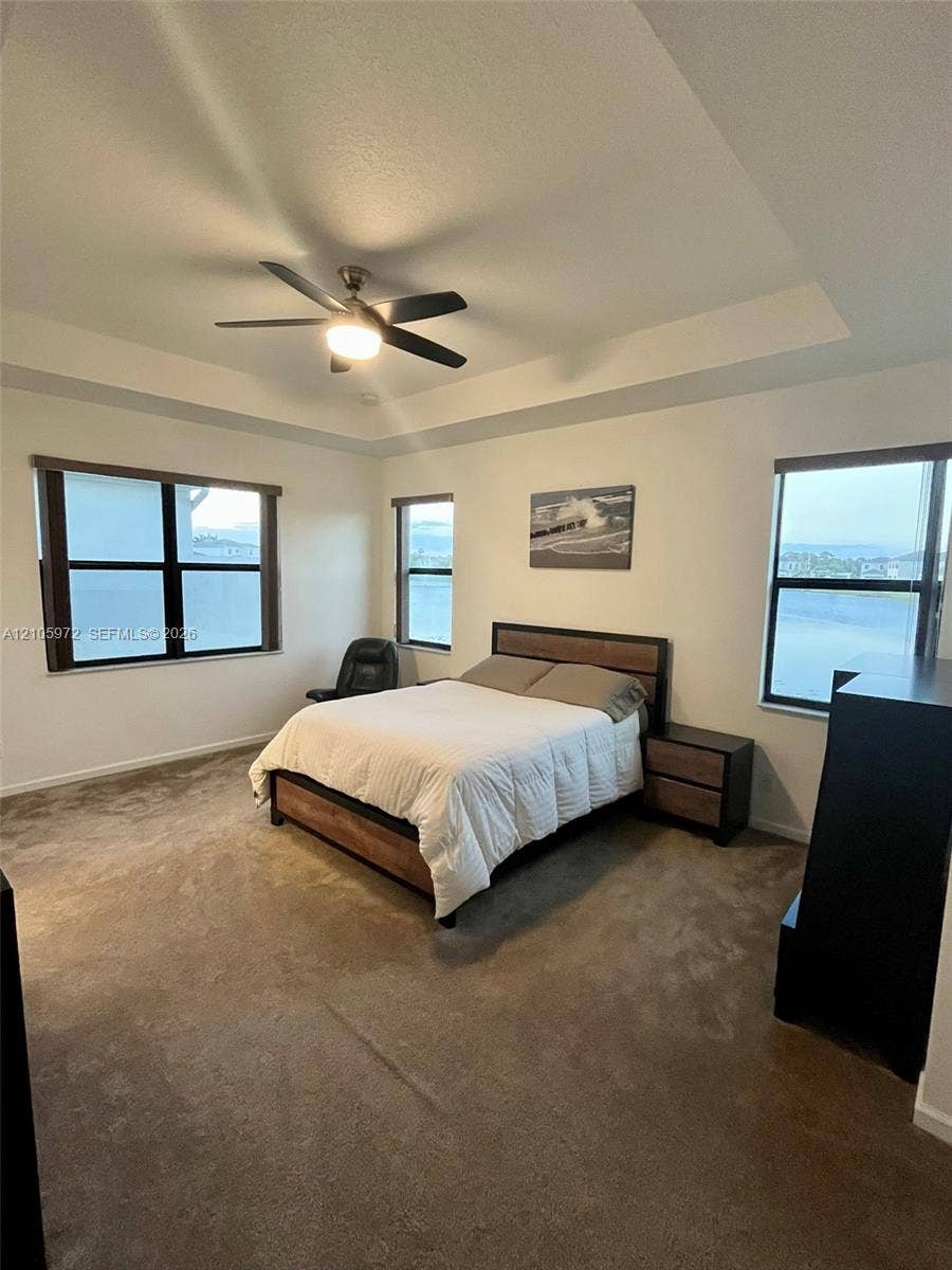 6220 Oceanaire Way, Lake Worth, FL 33467 Tray ceiling with a central fan, multiple windows with neutral roller shades, and wall-to-wall carpeting