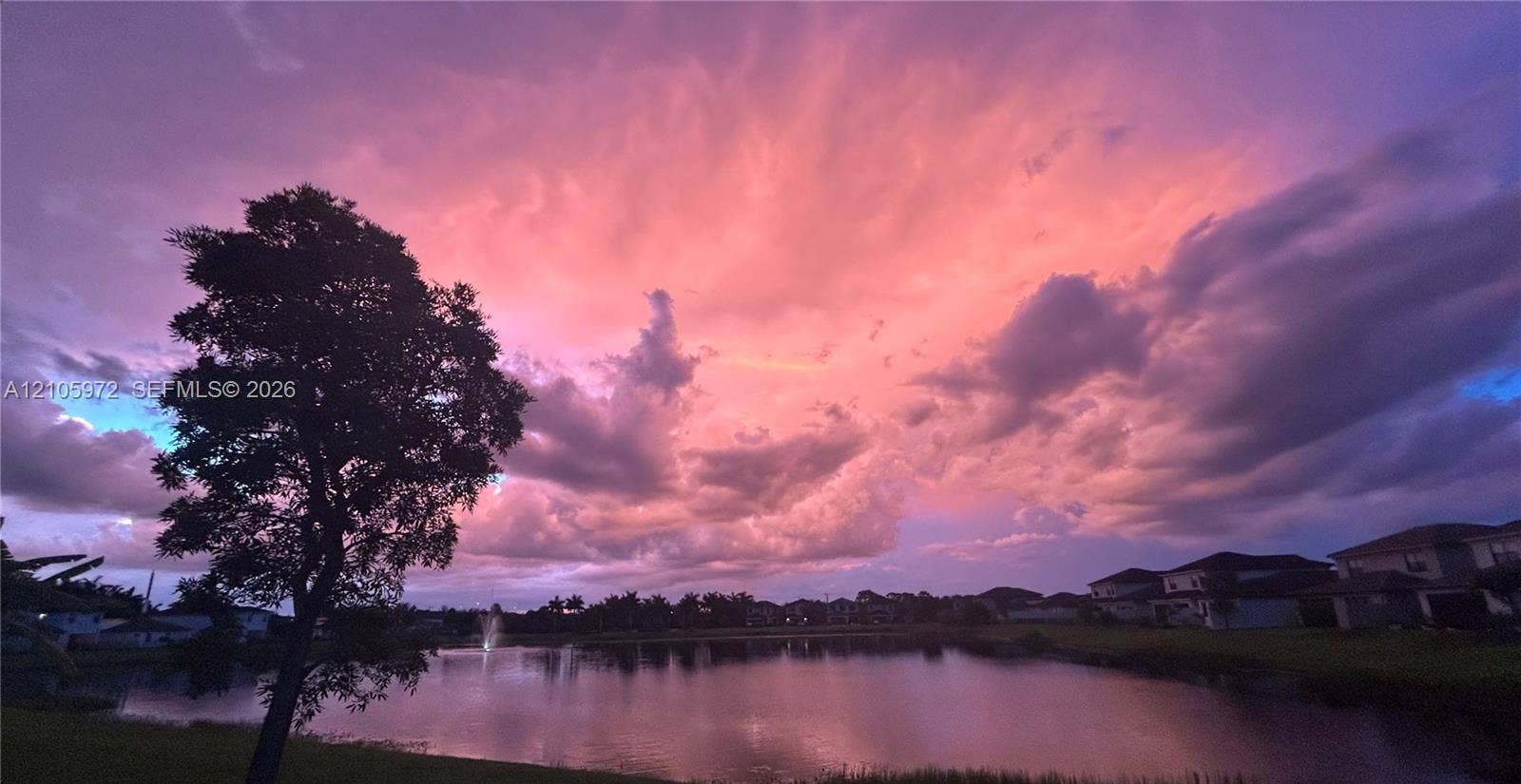 6220 Oceanaire Way, Lake Worth, FL 33467 Waterfront pond featuring fountain aerators and a silhouetted tree set against a backdrop of the sky