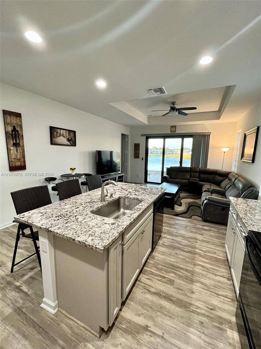 6220 Oceanaire Way, Lake Worth, FL 33467 Kitchen island featuring a stone countertop, undermount stainless steel sink, wood-finish flooring, recessed lighting, and tray ceiling