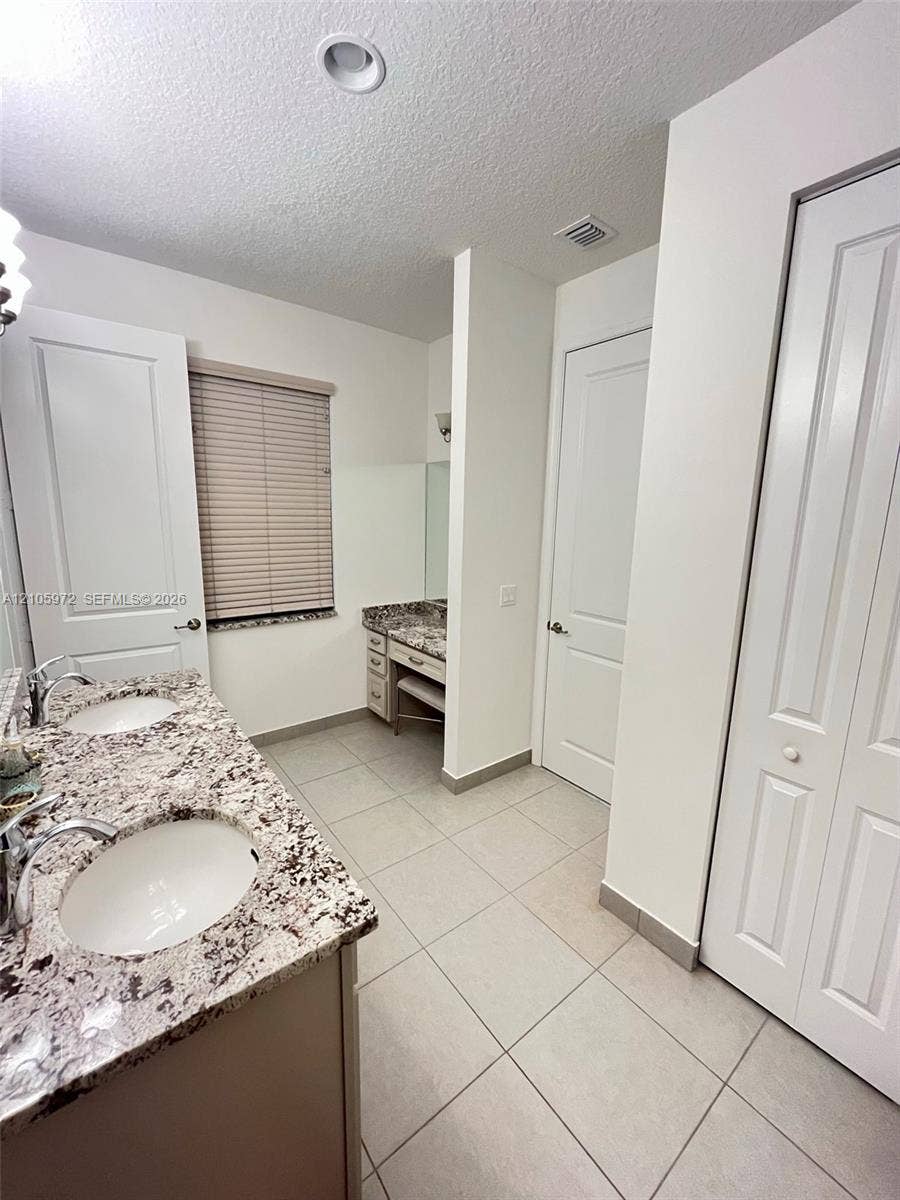 6220 Oceanaire Way, Lake Worth, FL 33467 Bathroom featuring a dual-sink vanity with stone-surface countertops, recessed lighting, tile flooring, and a dedicated vanity seating area with integrated cabinetry