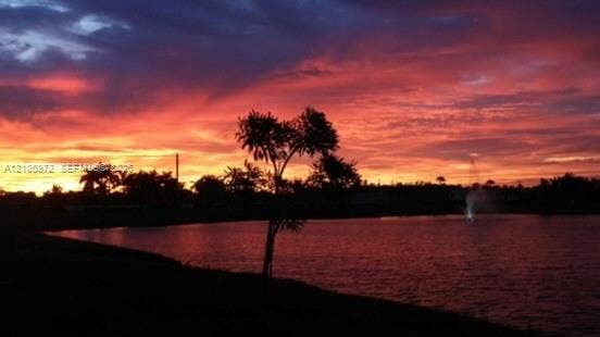 6220 Oceanaire Way, Lake Worth, FL 33467 Waterfront property featuring a pond, a central fountain, and mature tree silhouettes set against a prominent sunset backdrop