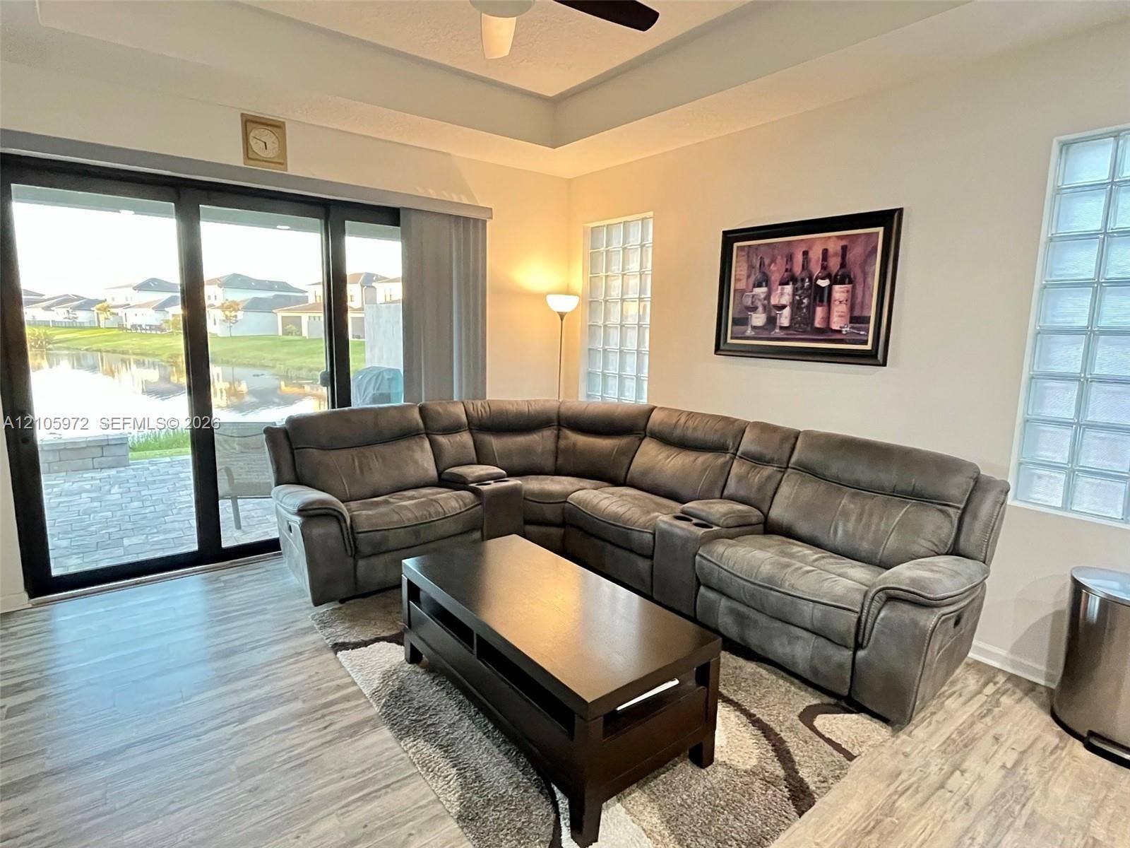 6220 Oceanaire Way, Lake Worth, FL 33467 Tray ceiling with integrated fan, wood-finish flooring, and glass block windows, featuring large sliding glass doors opening to a paved patio area