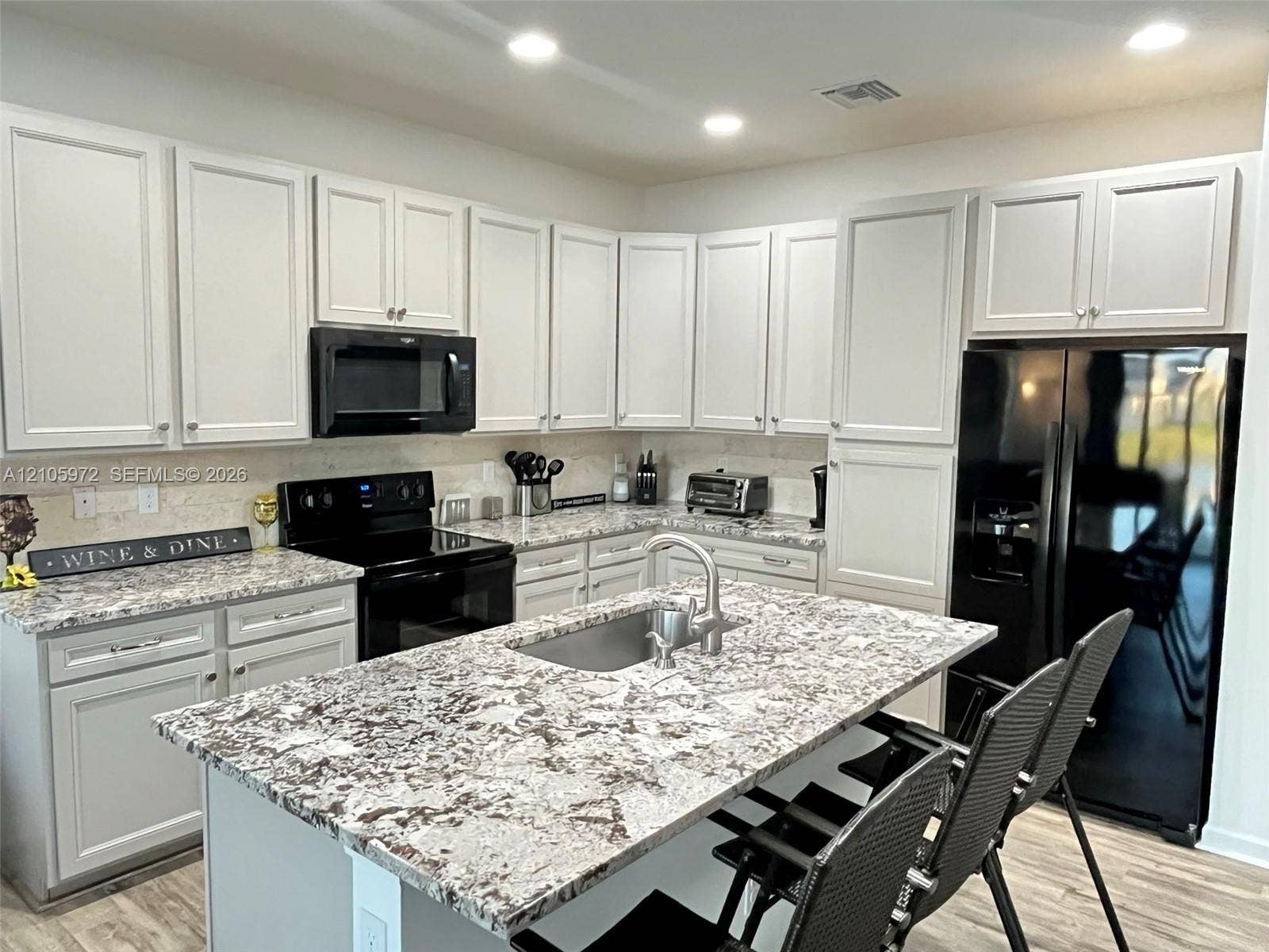 6220 Oceanaire Way, Lake Worth, FL 33467 Kitchen featuring light-toned cabinetry, patterned stone-finish countertops, central island with an undermount sink, recessed lighting, and black appliances