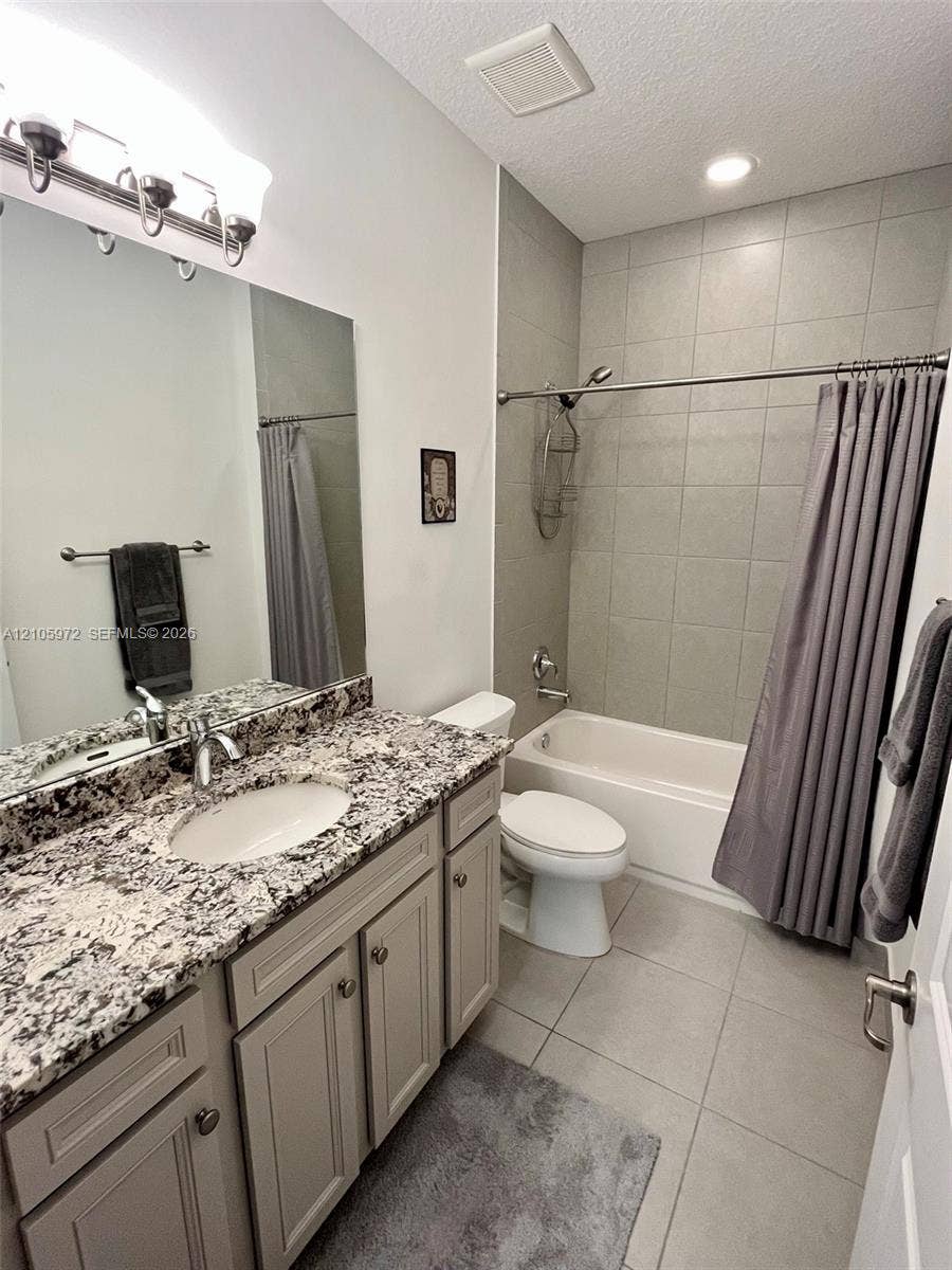 6220 Oceanaire Way, Lake Worth, FL 33467 Bathroom featuring light-toned cabinetry, patterned stone-finish countertop, undermount sink, large wall mirror, and tub-shower combination with tile surround