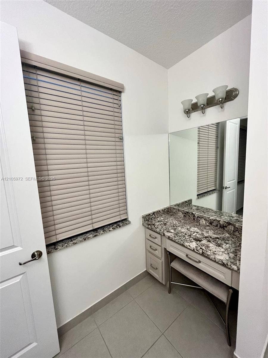 6220 Oceanaire Way, Lake Worth, FL 33467 Built-in vanity featuring a stone countertop, three-drawer cabinetry, large wall-mounted mirror, and three-bulb vanity lighting fixture
