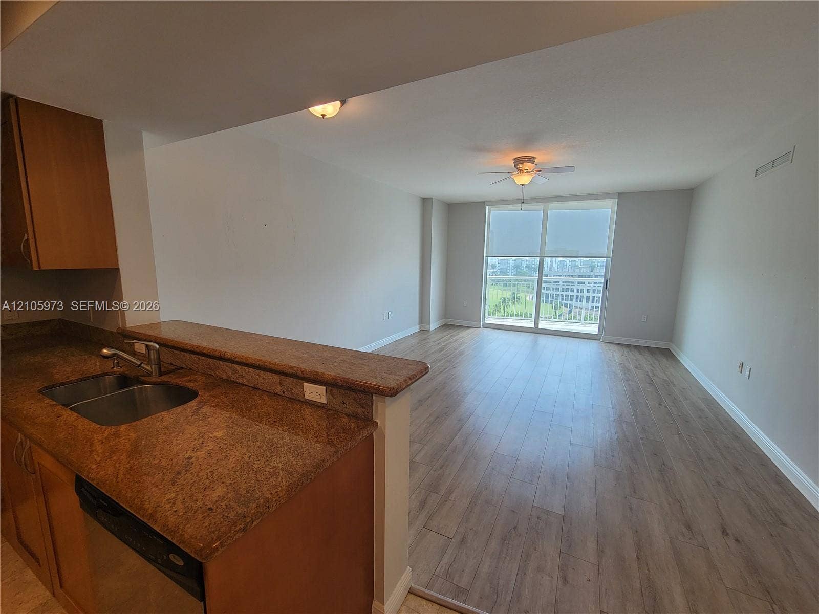 1755 E Hallandale Beach Boulevard, #704E, Hallandale Beach, Hallandale Beach, FL 33009 Kitchen featuring a breakfast bar, stone-surface countertops, dual-basin stainless steel sink, and wood-finish flooring extending into the main area with floor-to-ceiling glass sliding doors