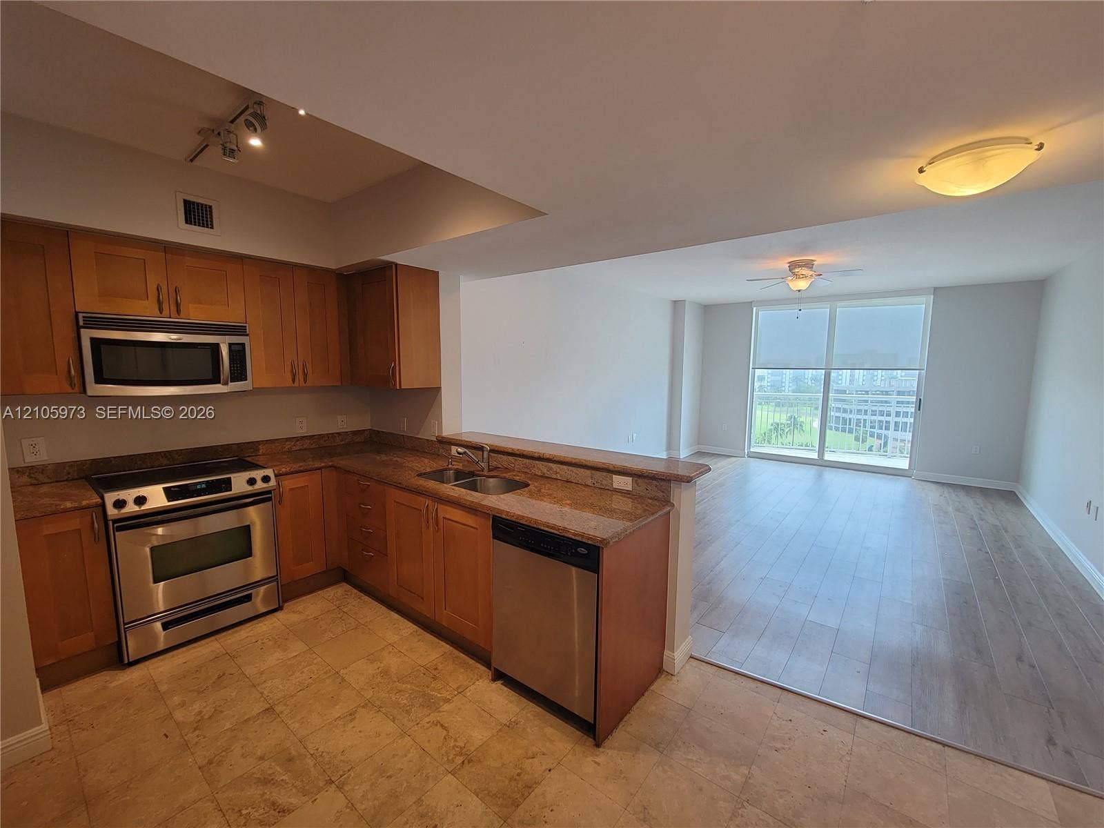 1755 E Hallandale Beach Boulevard, #704E, Hallandale Beach, Hallandale Beach, FL 33009 Kitchen featuring wood cabinetry, stone countertops, stainless steel appliances, and tile flooring, opening to a space with wood-finish flooring and floor-to-ceiling windows