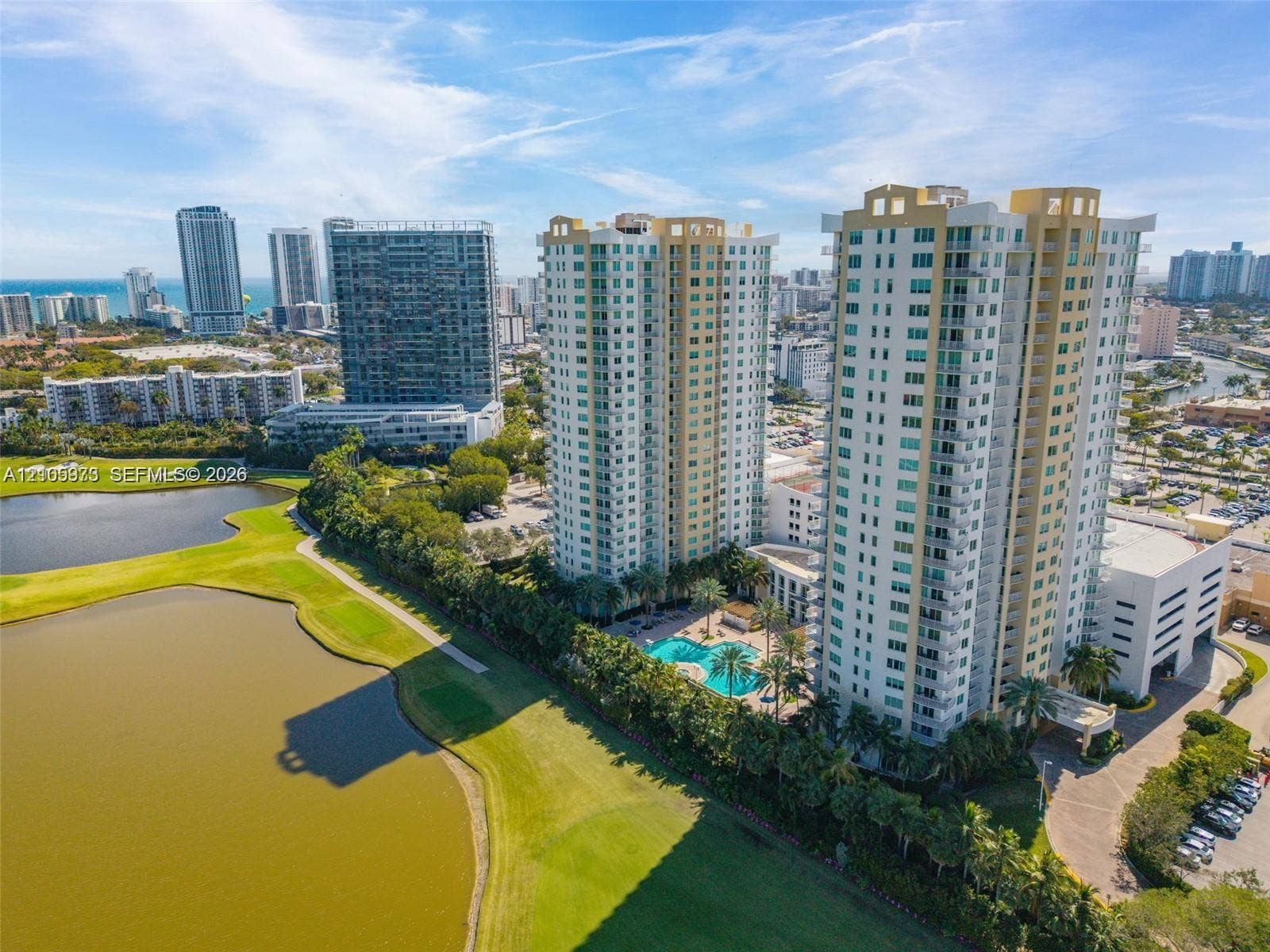 1755 E Hallandale Beach Boulevard, #704E, Hallandale Beach, Hallandale Beach, FL 33009 High-rise residential towers featuring balconies, ground-level swimming pool, and dedicated parking structure, positioned along a water feature and golf course