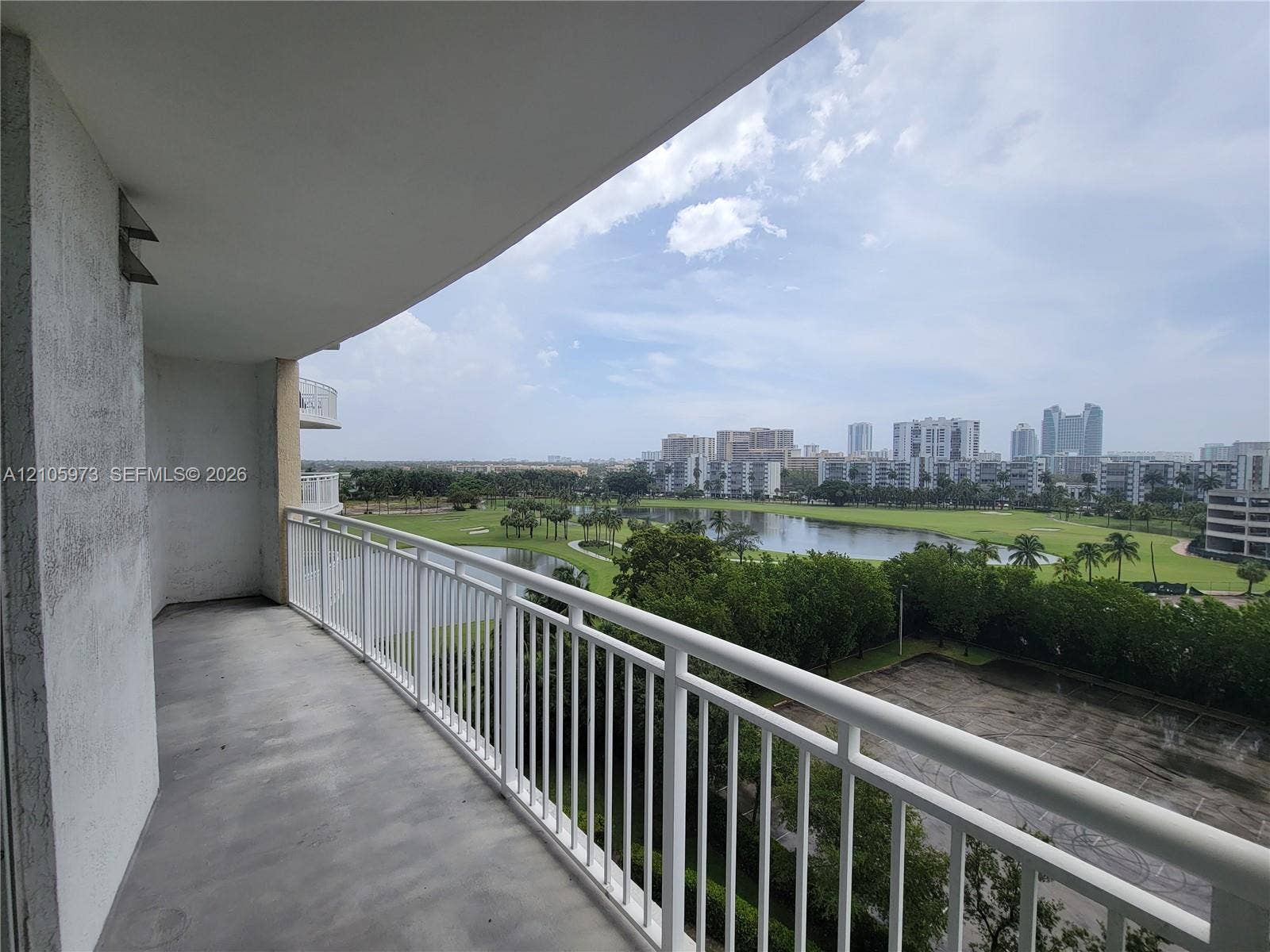 1755 E Hallandale Beach Boulevard, #704E, Hallandale Beach, Hallandale Beach, FL 33009 Covered balcony featuring concrete flooring and a white metal railing, overlooking a landscaped water feature and surrounding cityscape