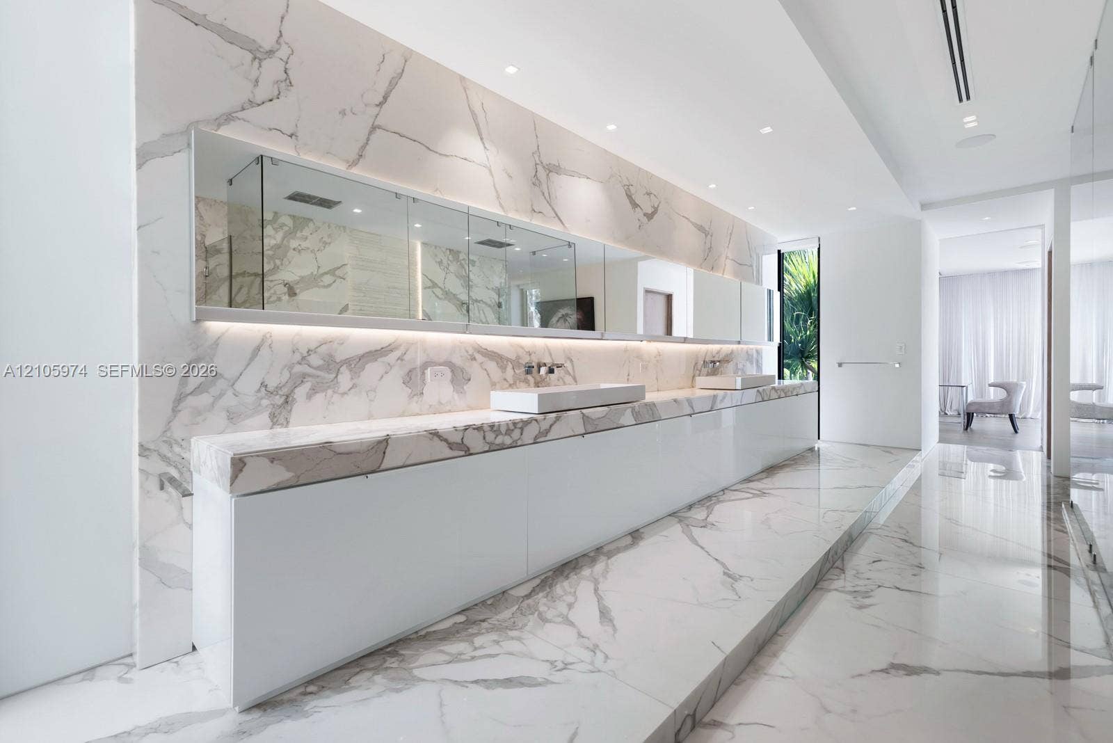 4395 Pine Tree Drive, Miami Beach, FL 33140 Large-format stone wall and floor tiling featuring prominent veining, integrated full-width vanity mirror with recessed lighting, and wall-mounted faucets over dual rectangular vessel sinks