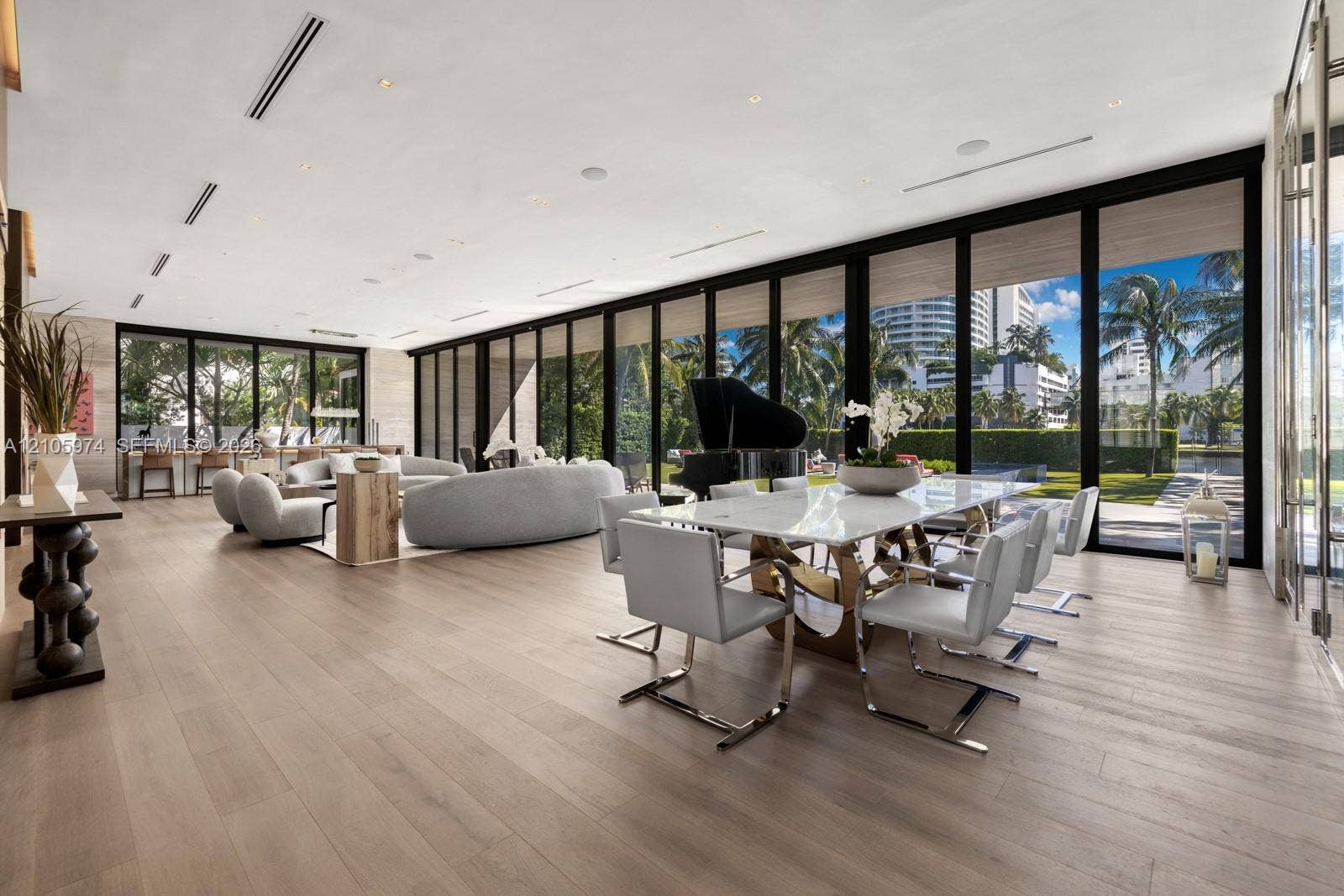 4395 Pine Tree Drive, Miami Beach, FL 33140 Open-concept living space featuring wood-finish flooring, floor-to-ceiling glass panel walls, recessed linear lighting, and built-in ceiling speakers